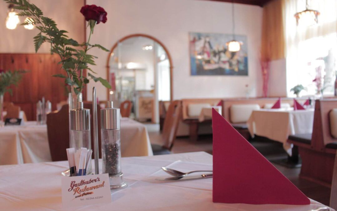 Interior view of a cozy restaurant with laid tables, red napkins and a rose in a vase.
