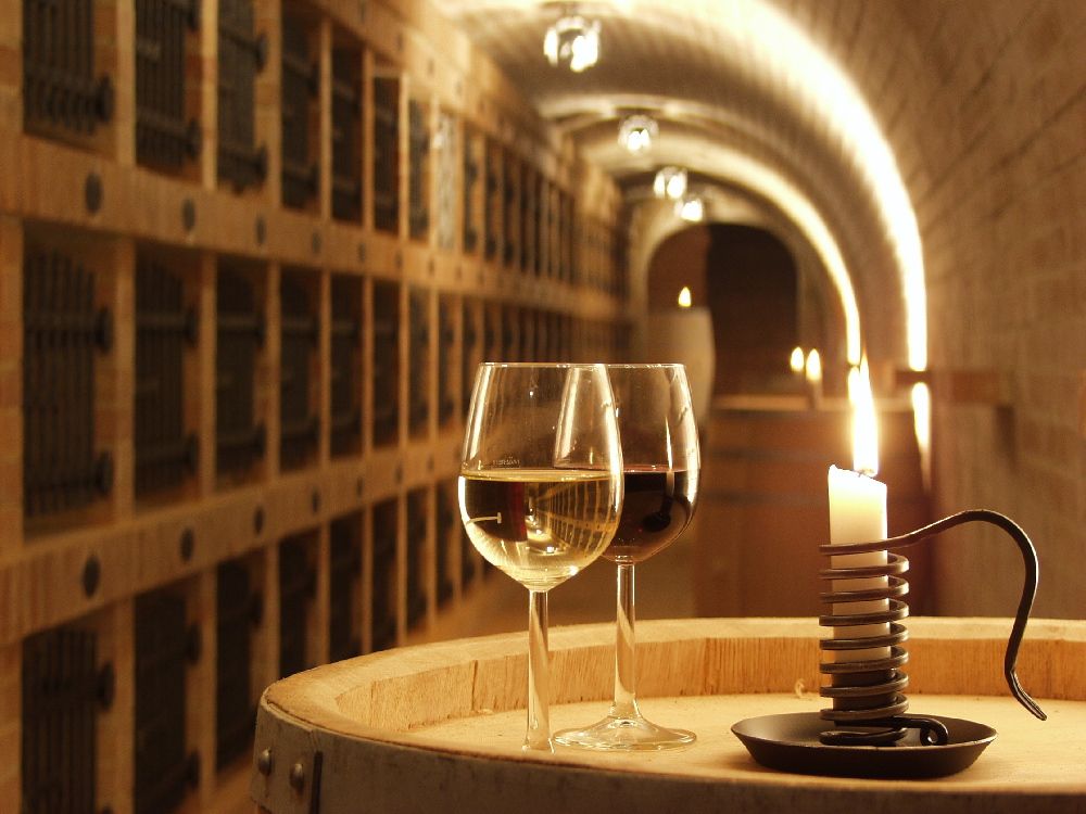 Two wine glasses and a candle on a barrel in a wine cellar.