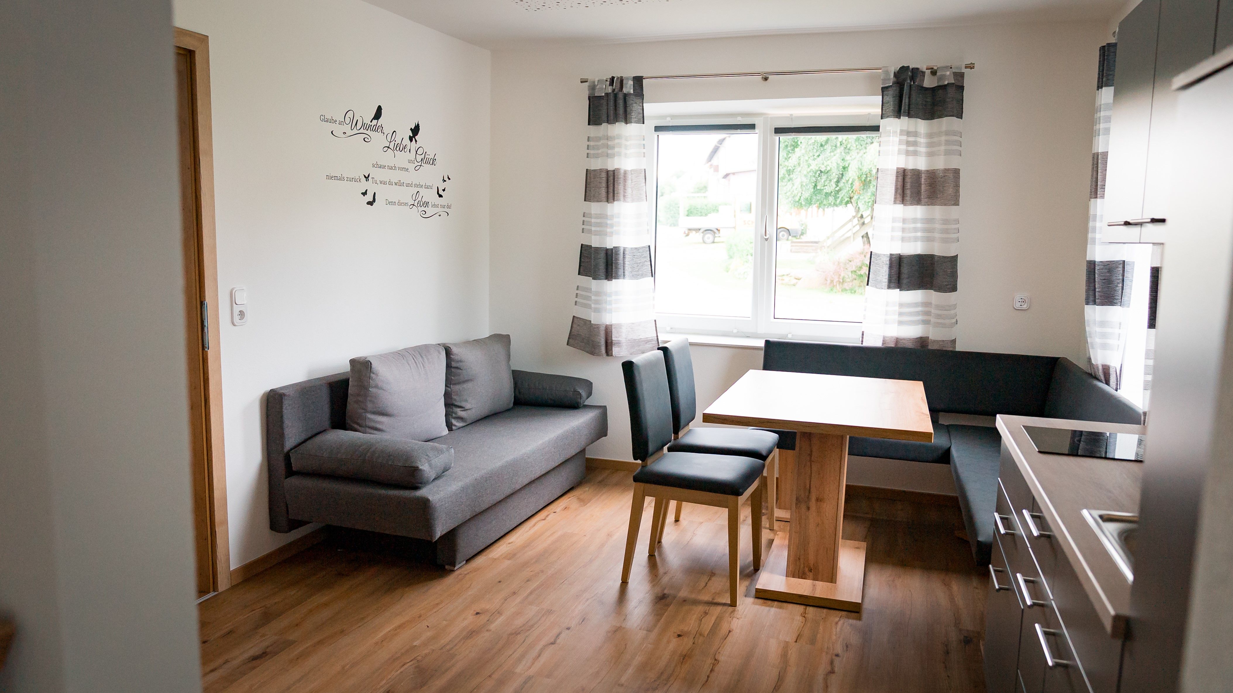 Modern kitchen with gray sofa, wooden table and chairs, window with curtains.