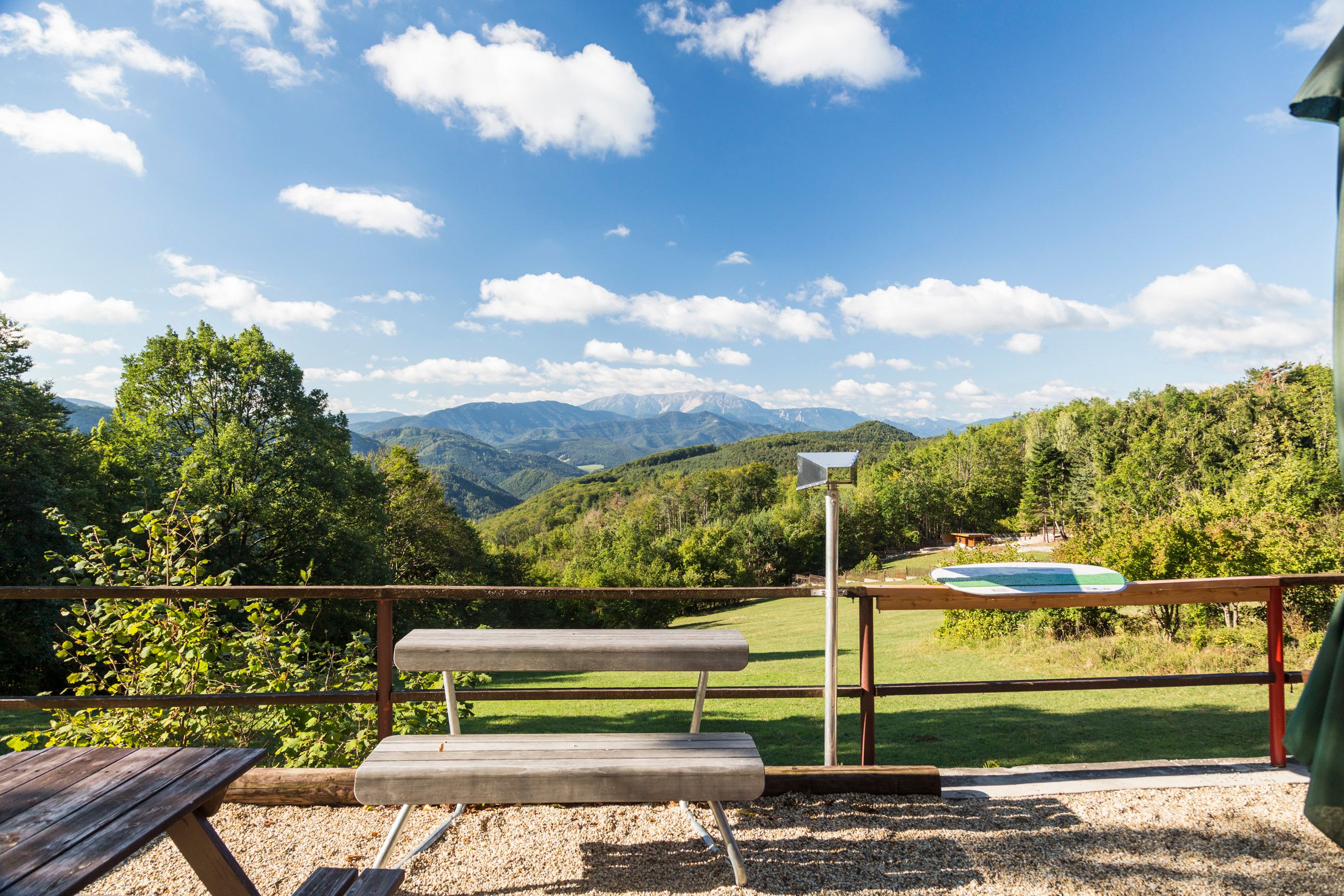 View from the Waxeneckhaus of wooded hills and mountains under a blue sky with clouds.