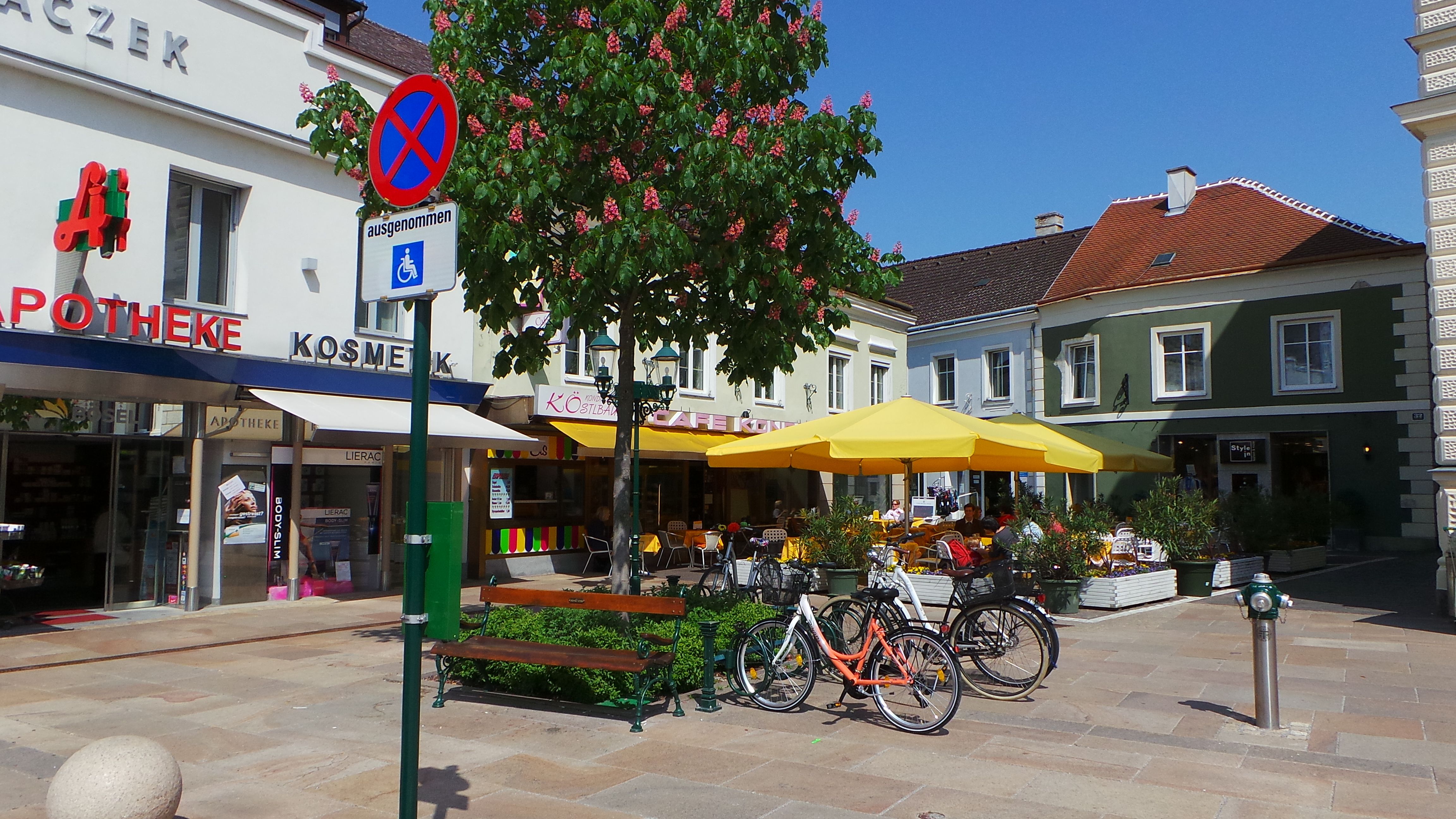 Street scene with pharmacy, café and yellow parasols.