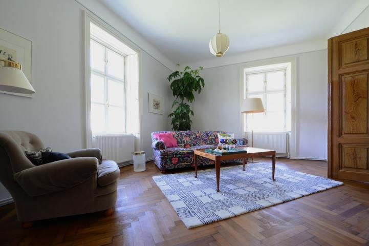 Living room with colorful sofa, armchair, carpet and plants.