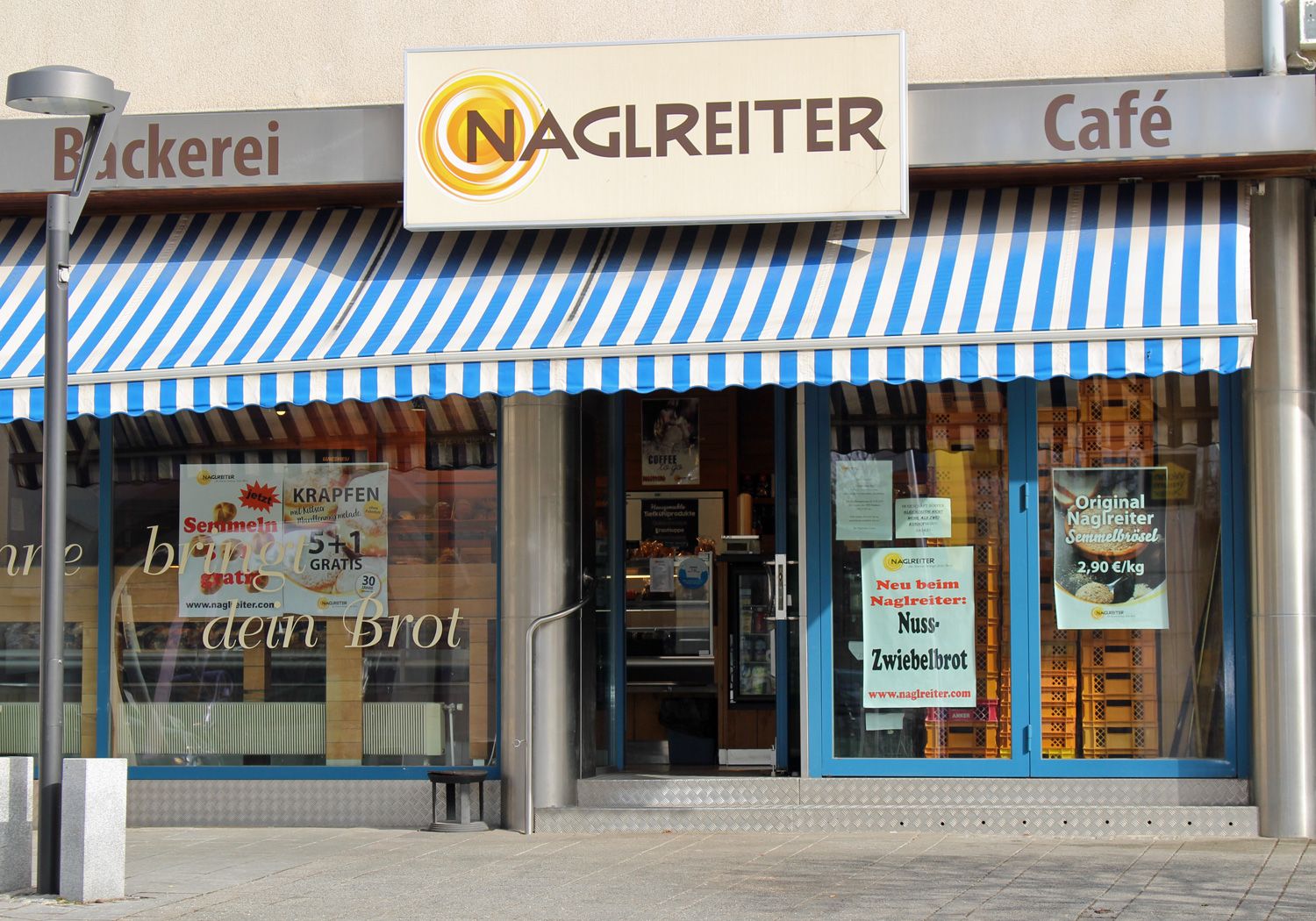 Entrance of a bakery with blue and white striped awning and signs for special offers.