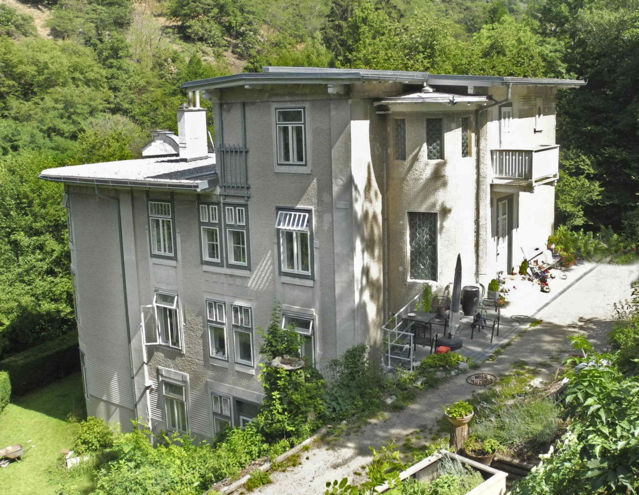 Large, multi-storey house with gray facade, surrounded by trees and garden.