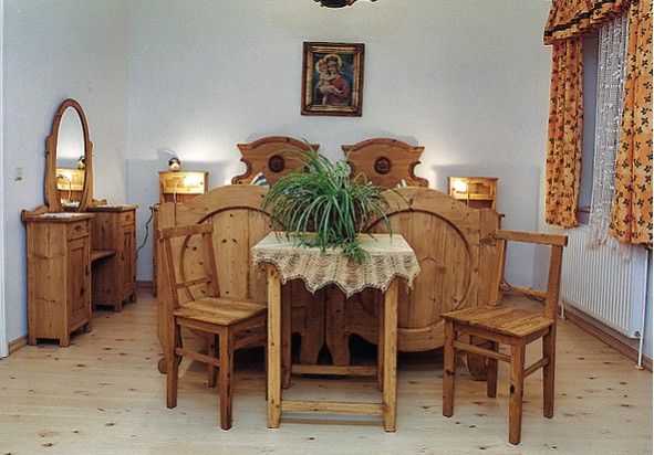 Rustic bedroom with wooden furniture, a double bed, a table with a plant and a mirror.