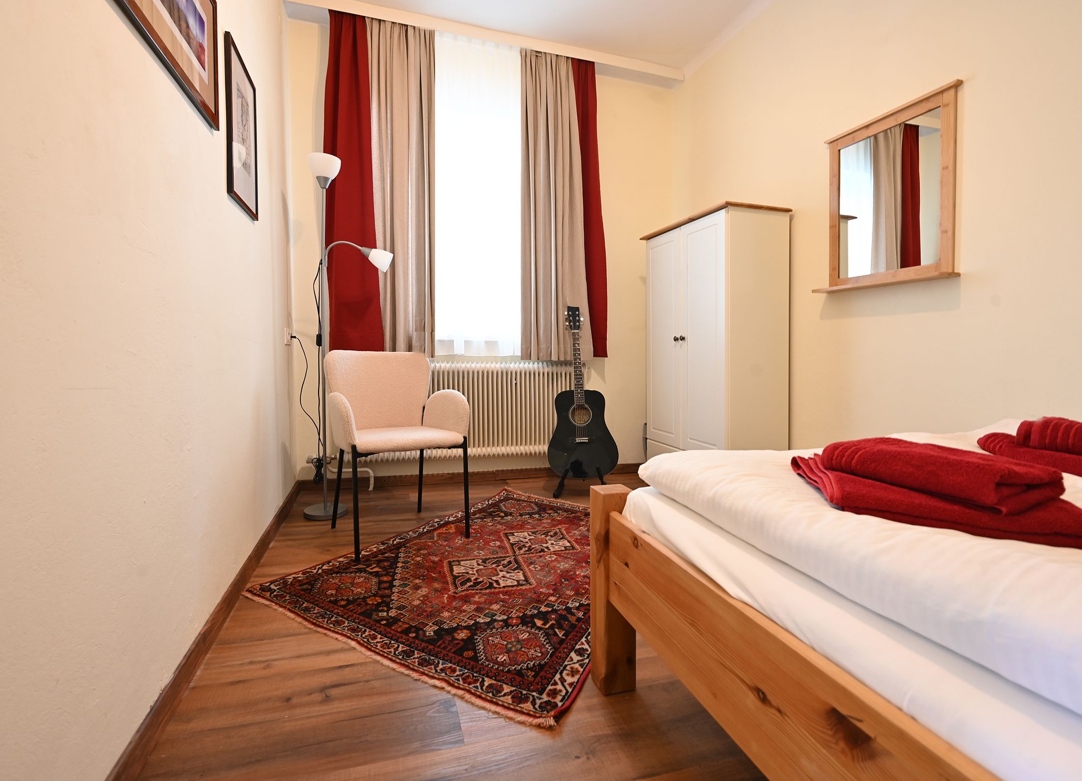 Small room with bed, carpet, chair, floor lamp, guitar and wardrobe.