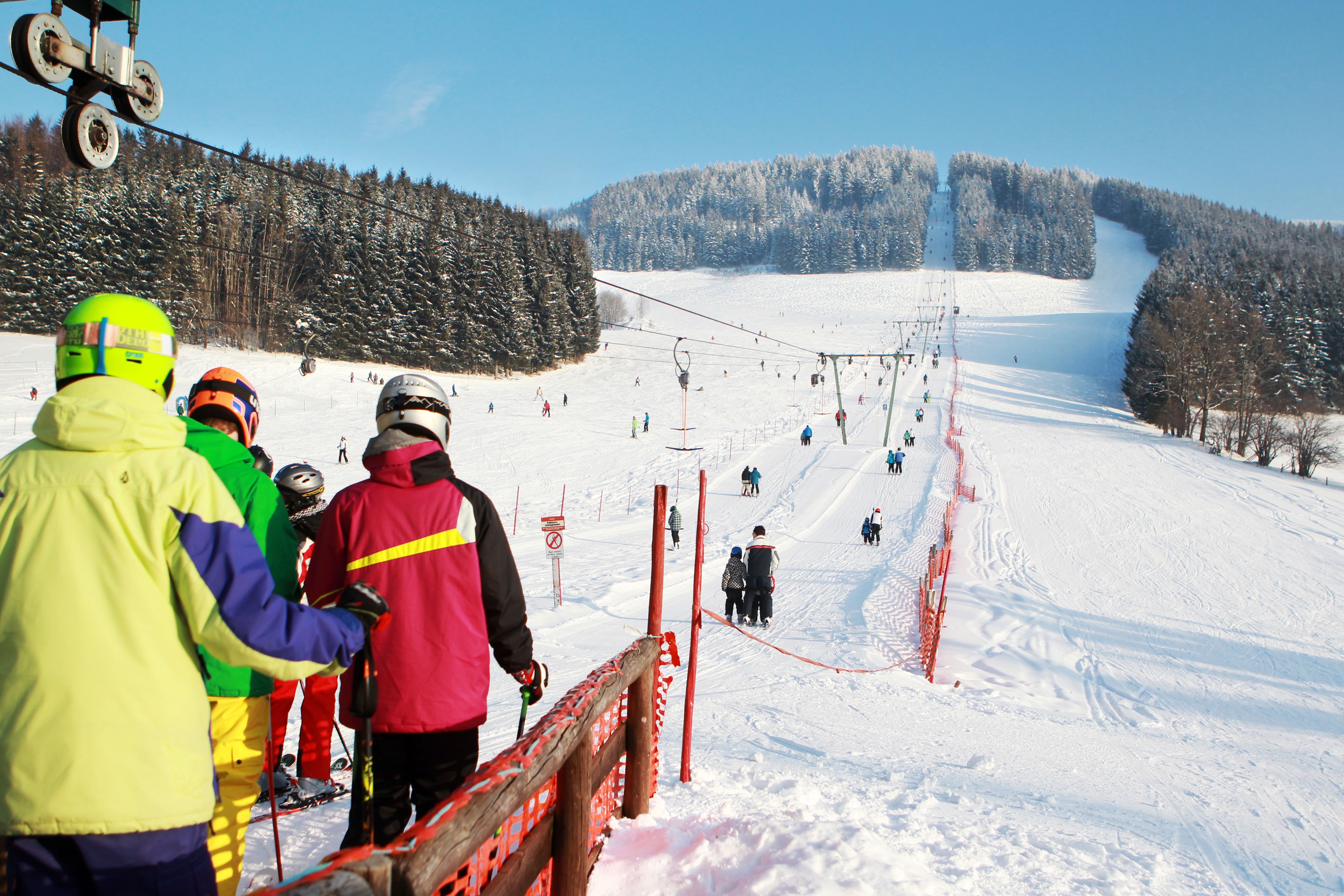 Skiers stand in a queue at the ski lift on a snowy slope.