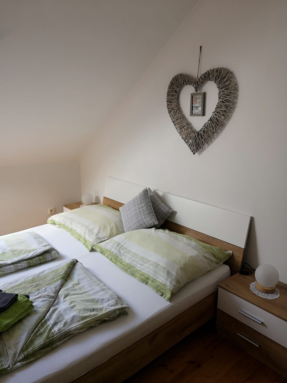Bedroom with double bed, green bed linen and heart-shaped wall decoration.