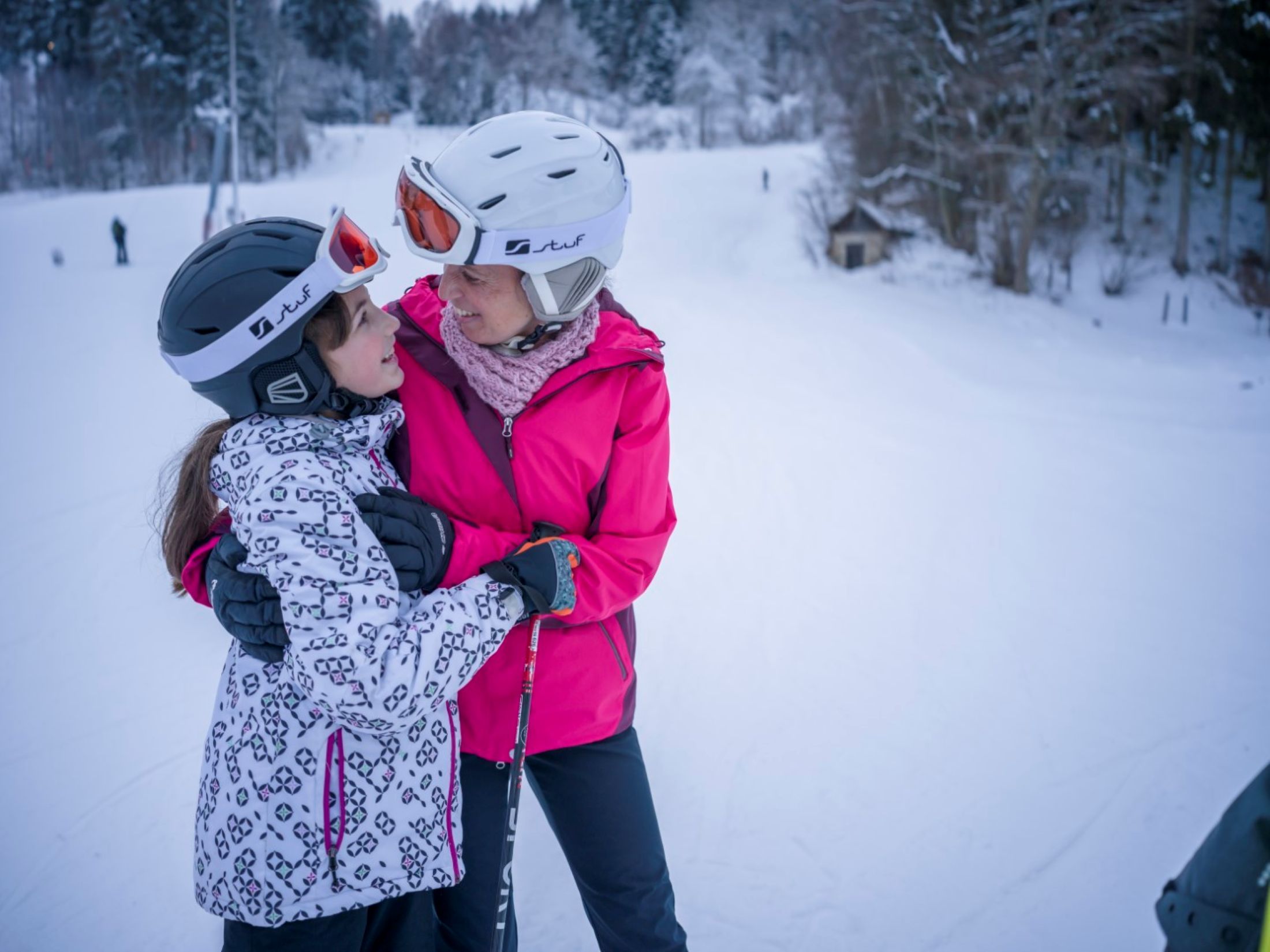 Two people in ski equipment embrace on a ski slope.