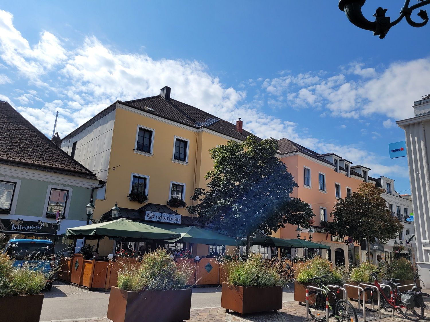 Street scene with yellow building, café with parasols and bicycles in the foreground.