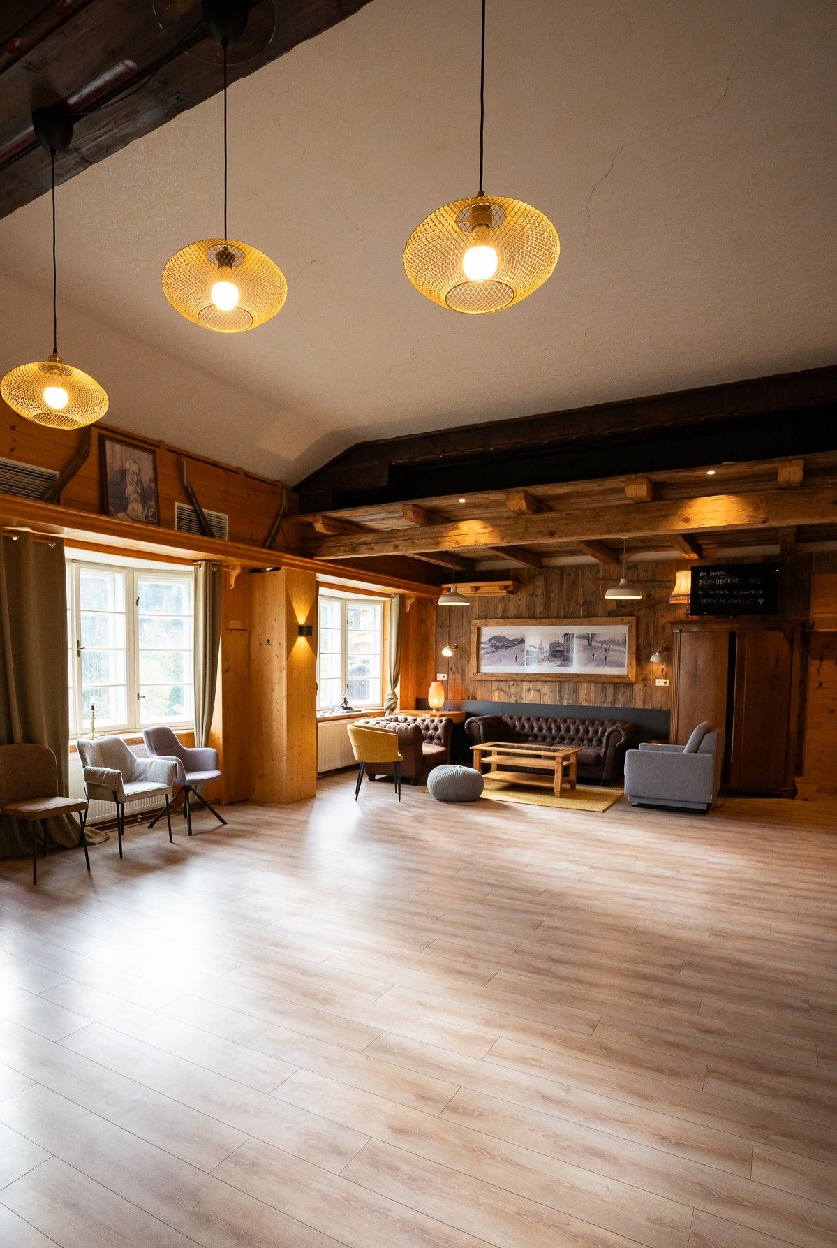 An interior view of a cozy room with a wooden floor, a leather sofa, and several chairs. Pendant lights illuminate the room.
