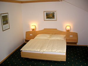 A simply furnished hotel room with a double bed, two bedside lamps and pictures on the wall.