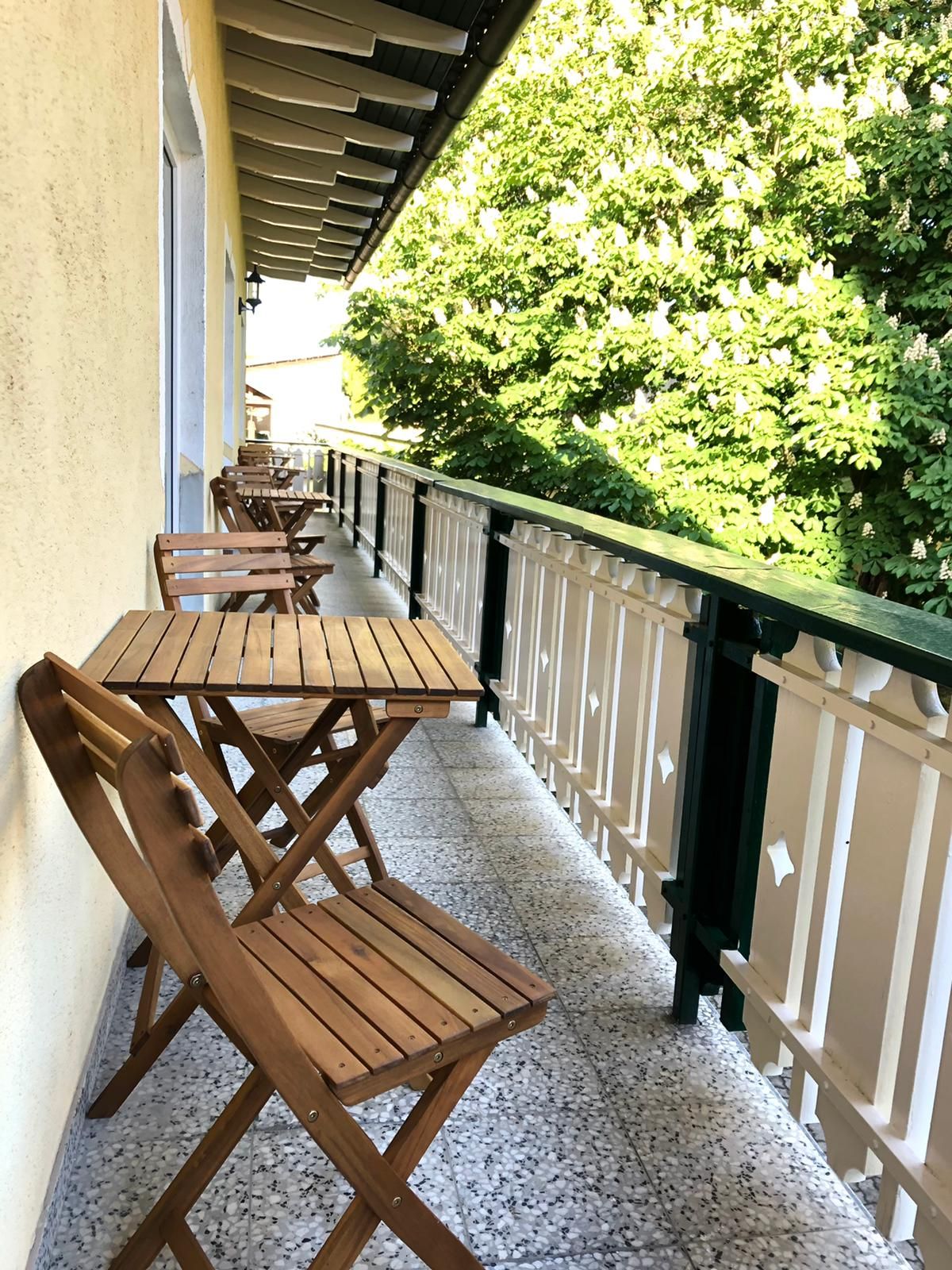 Wooden balcony with table and chairs, green trees next to it.
