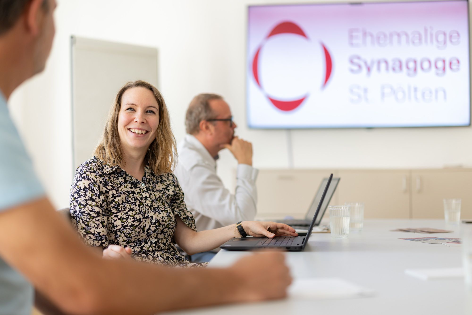 People in a seminar room at the Former Synagogue St. Pölten, sitting at a table with laptops.