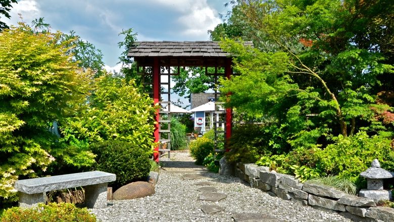 A Japanese garden with a red torii, surrounded by green plants and a gravel path.