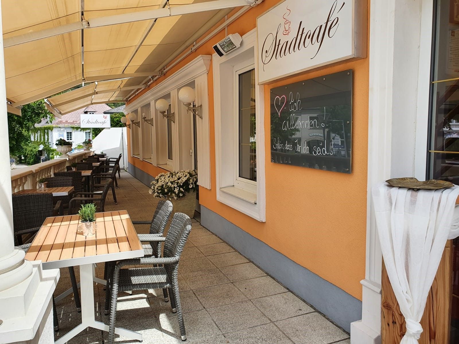 Outdoor area of a café with tables and chairs, orange wall with sign 'Stadtcafé'.