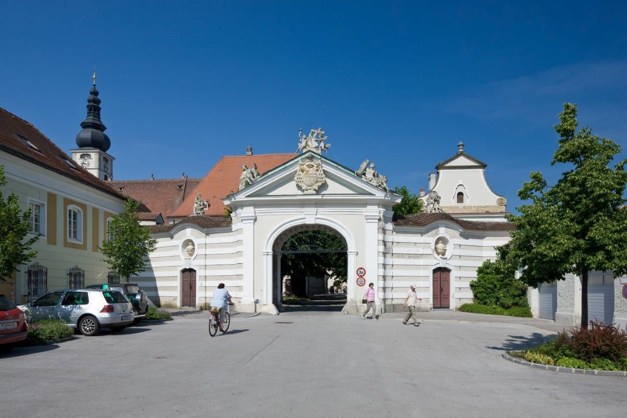 Historic diocese building with archway and church tower in the background.