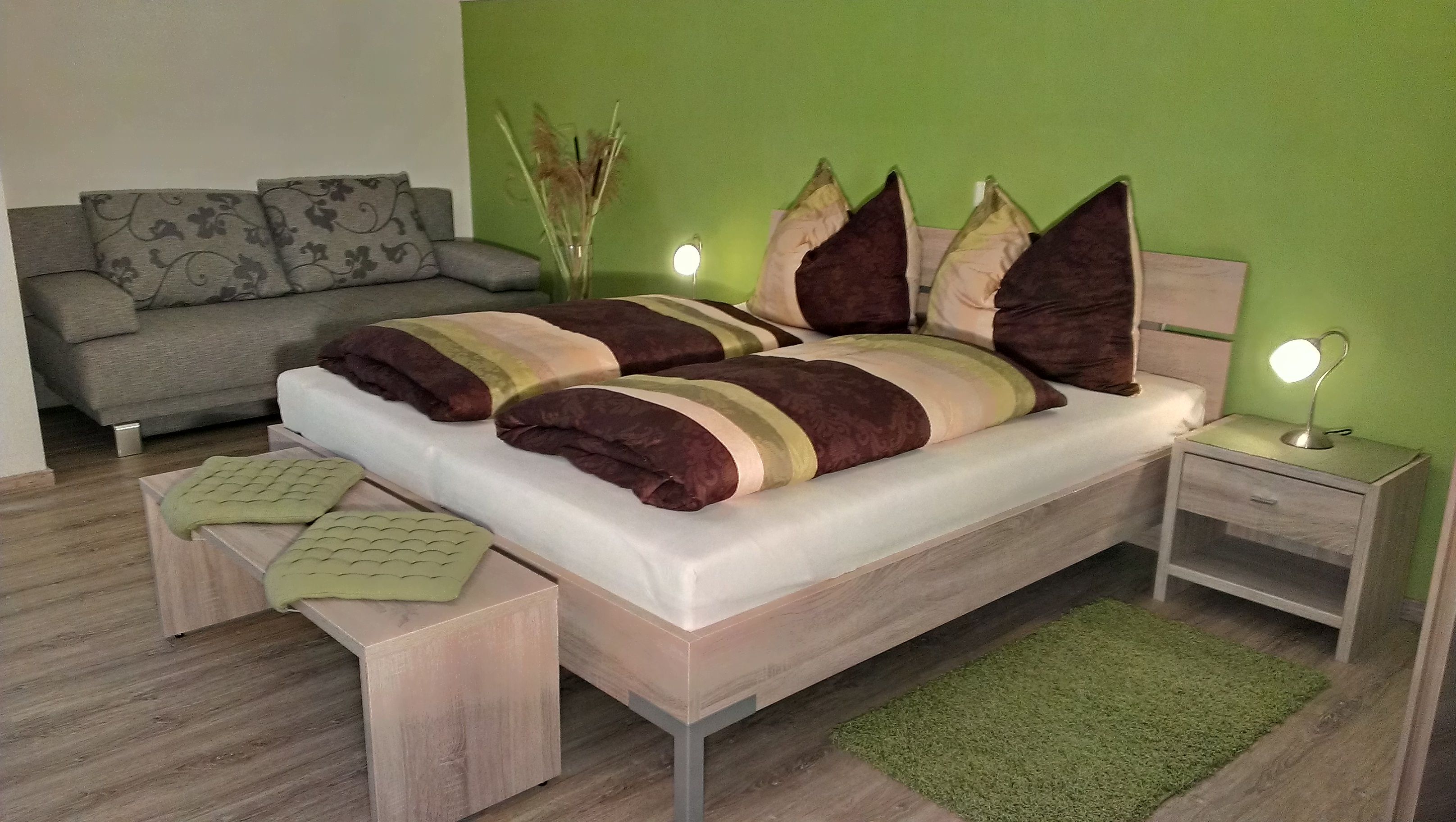 Cozy bedroom with green painted wall, double bed, bedside lamps and gray sofa.