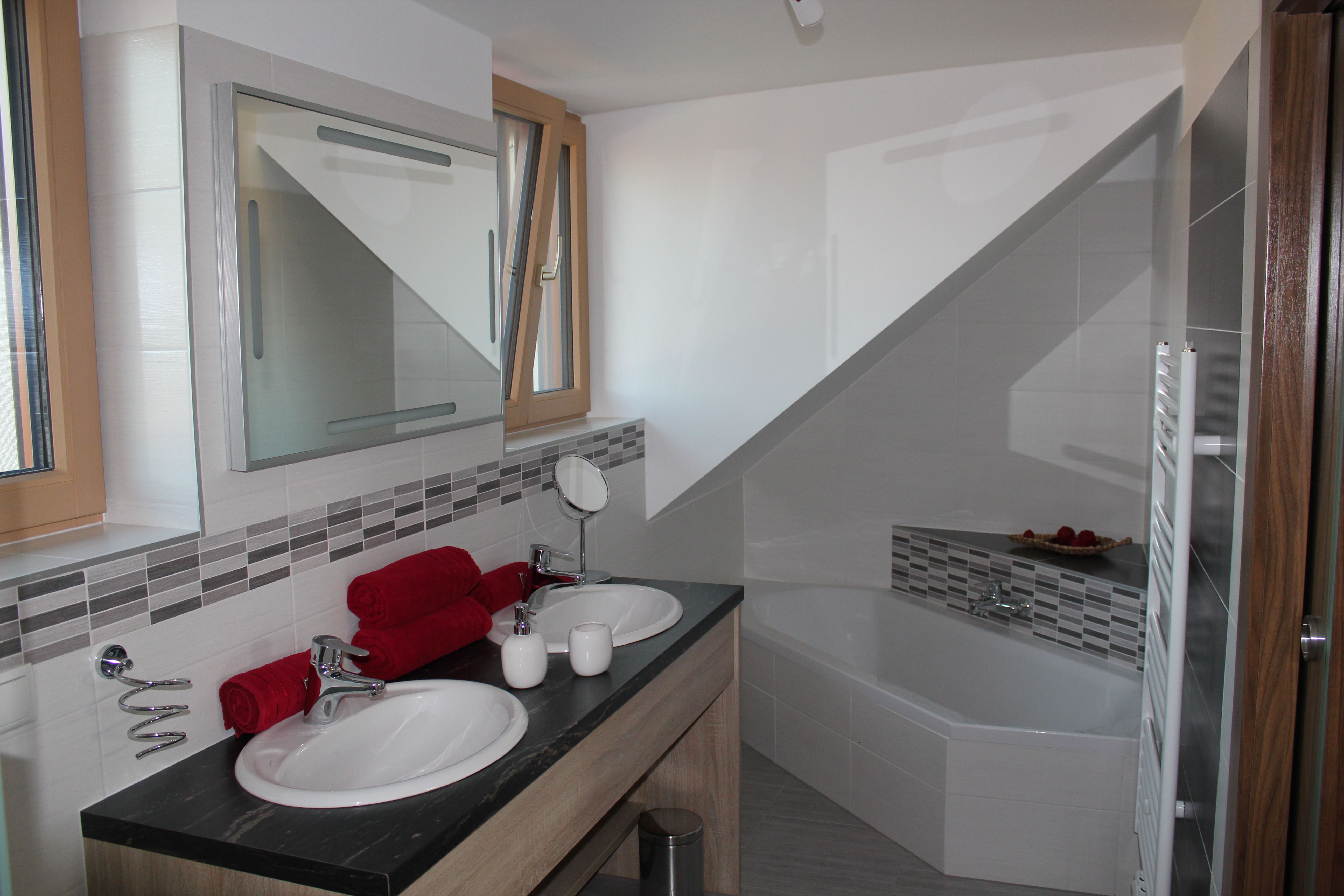 Modern bathroom with double washbasin, bathtub and red towels.