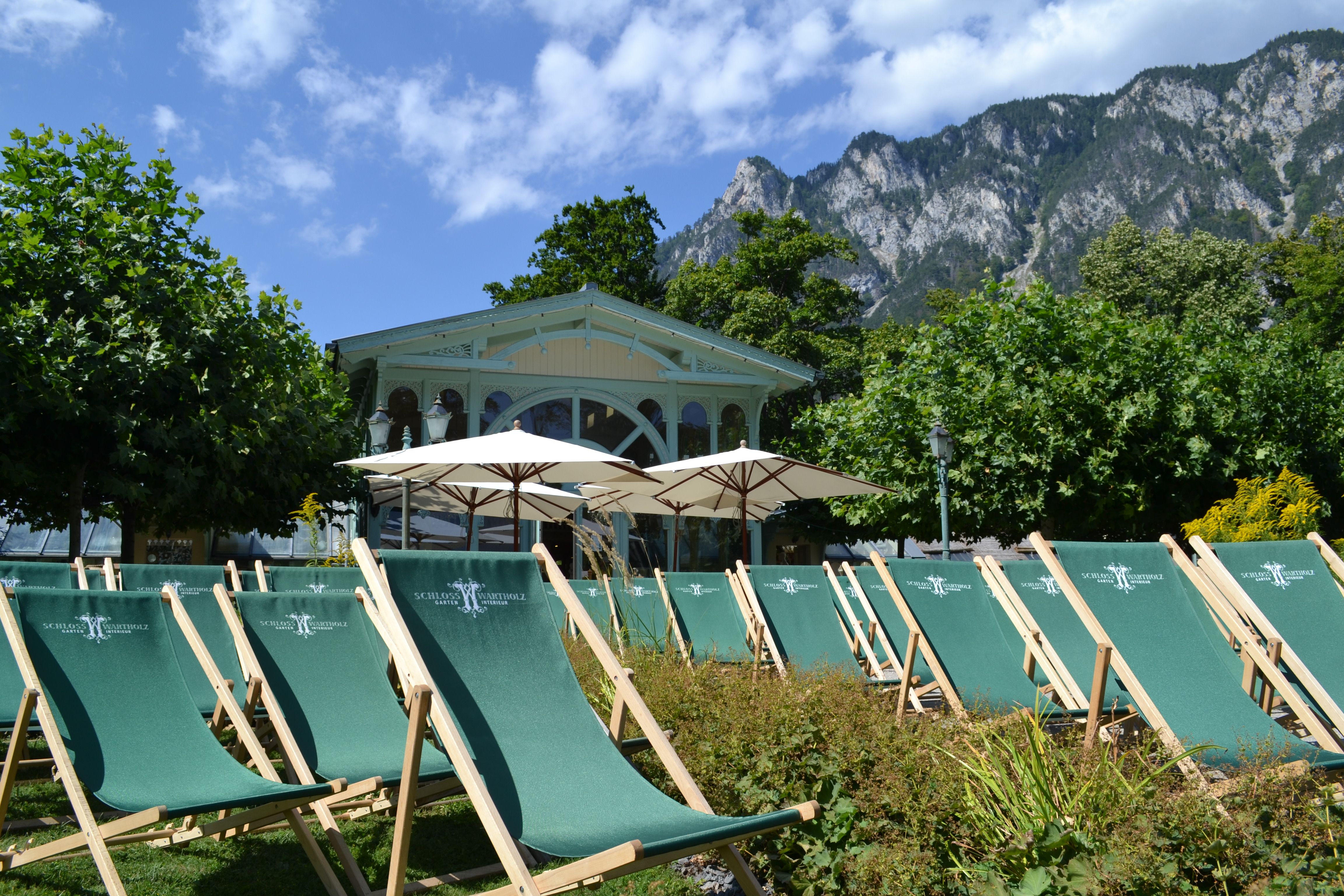 Green deckchairs in front of a pavilion with mountains in the background.