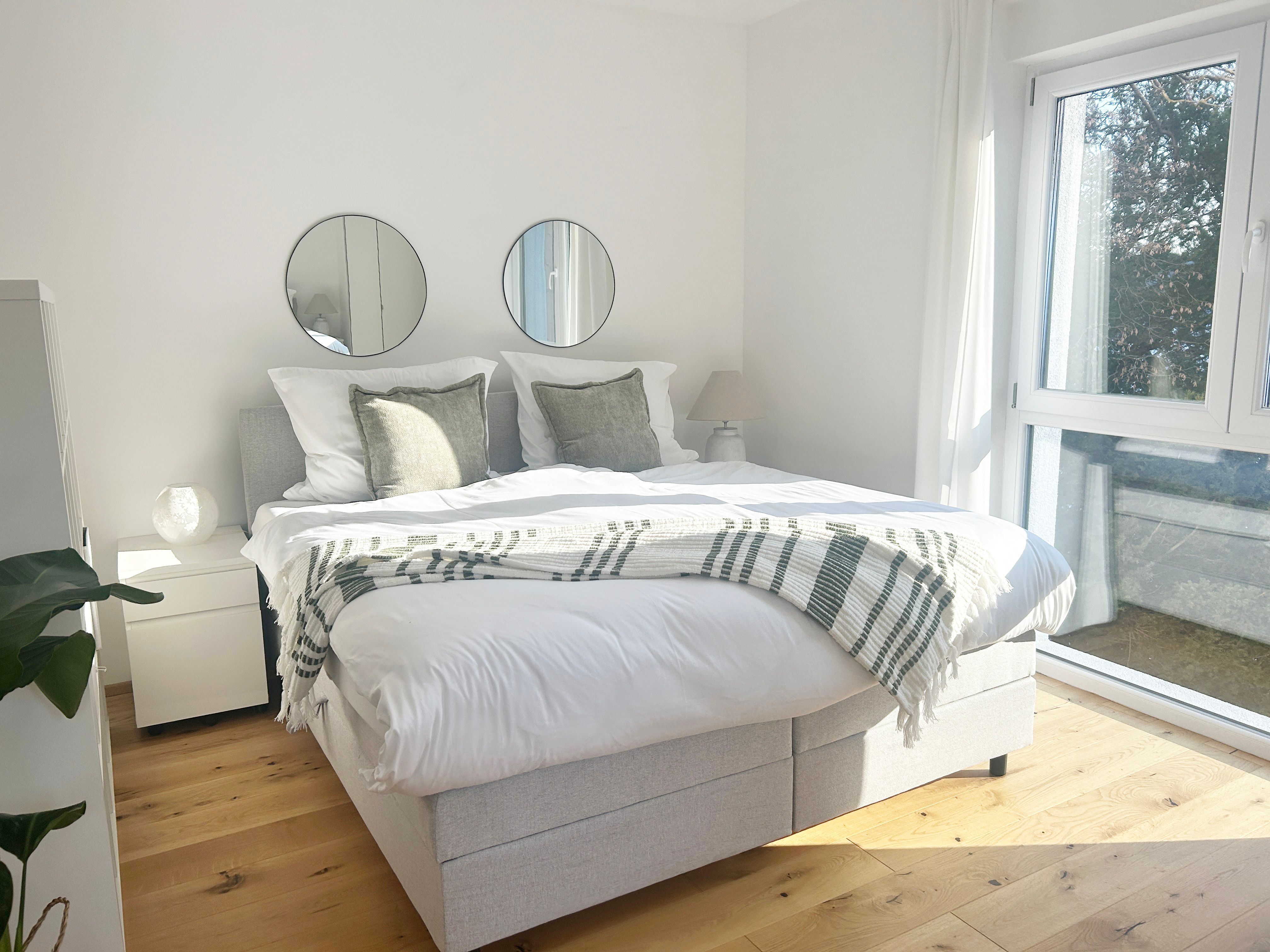 Bright bedroom with double bed, two round mirrors on the wall and large windows.