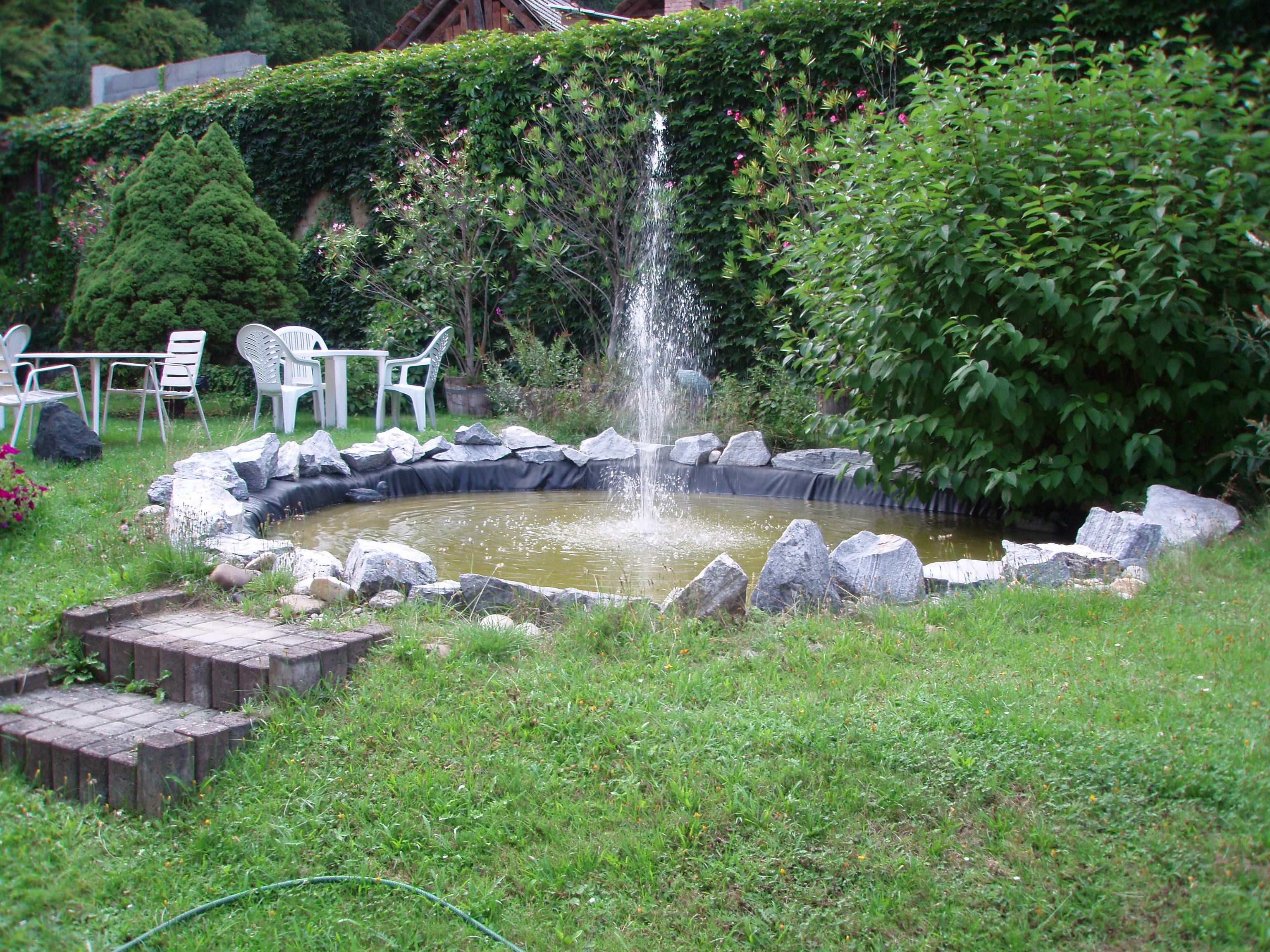 Garden with small pond and fountain, surrounded by plants and garden furniture.