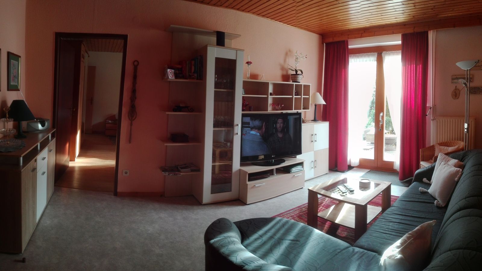 Cozy living room with sofa, TV, shelf and glass door with red curtains.