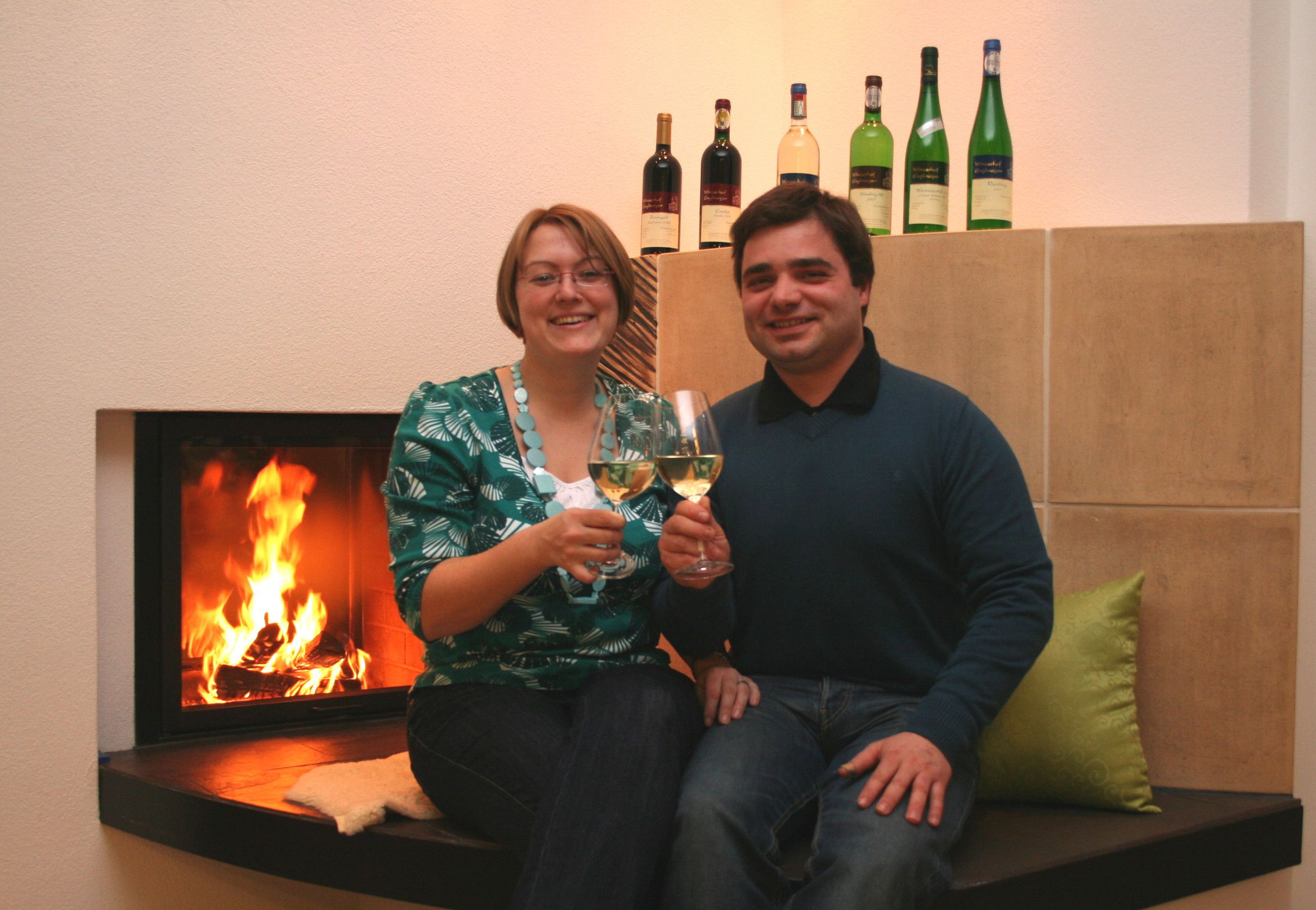 A couple is sitting in front of a fireplace, clinking glasses of wine.