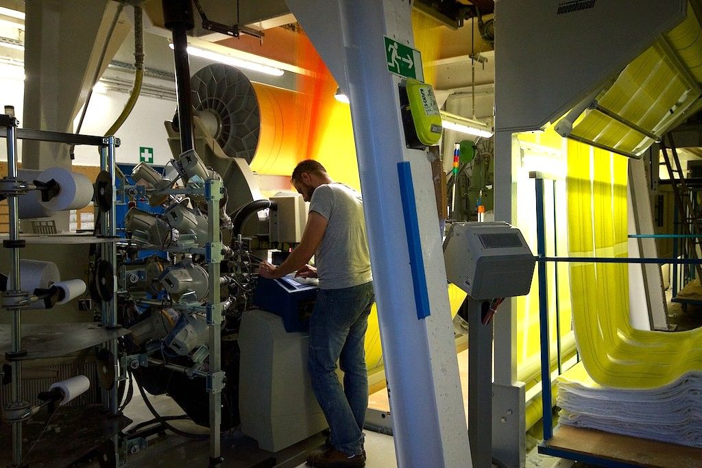 A man works on a machine in a factory with yellow and orange fabric panels.