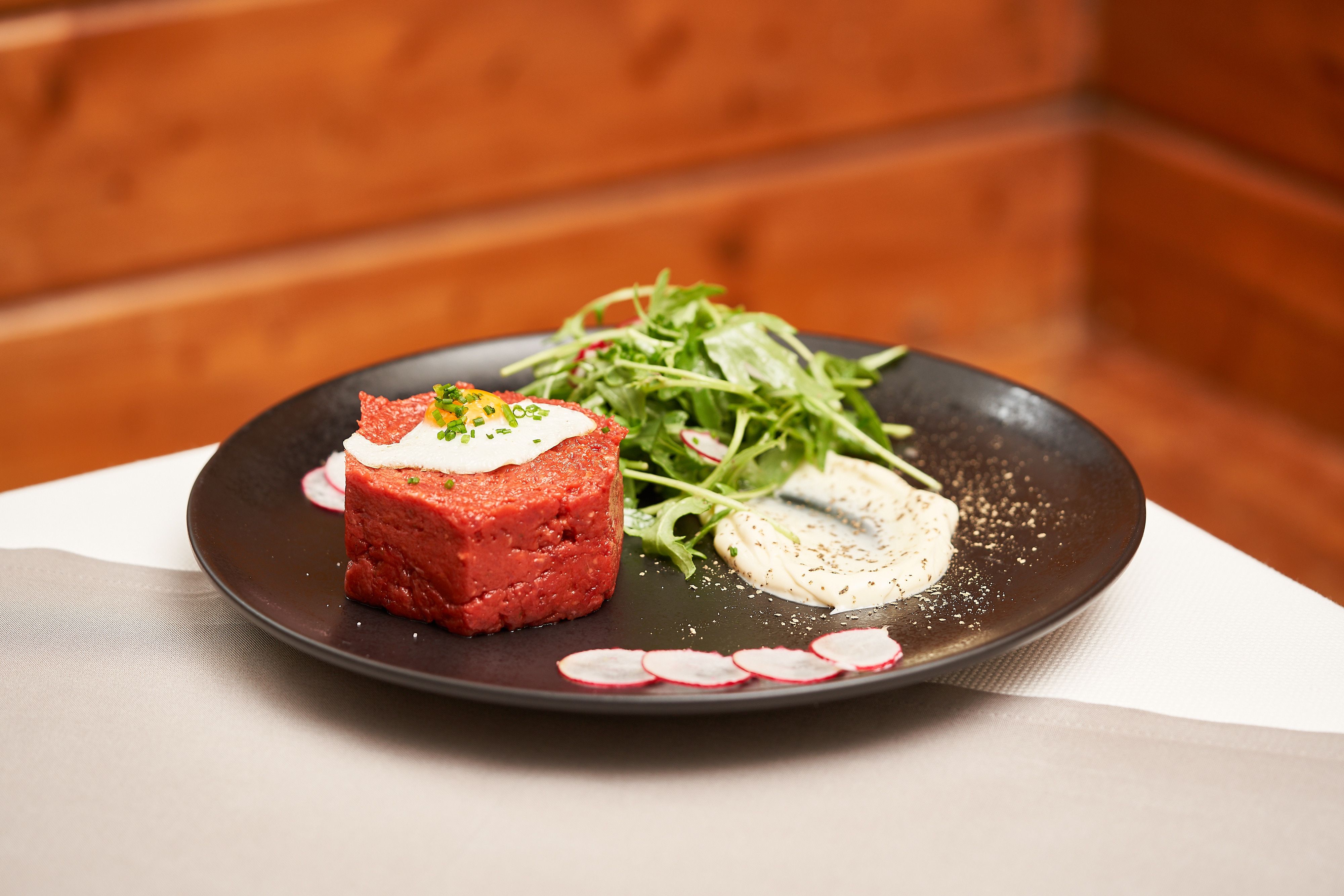 A plate with beef tartare, salad and sauce, decorated with radish slices.