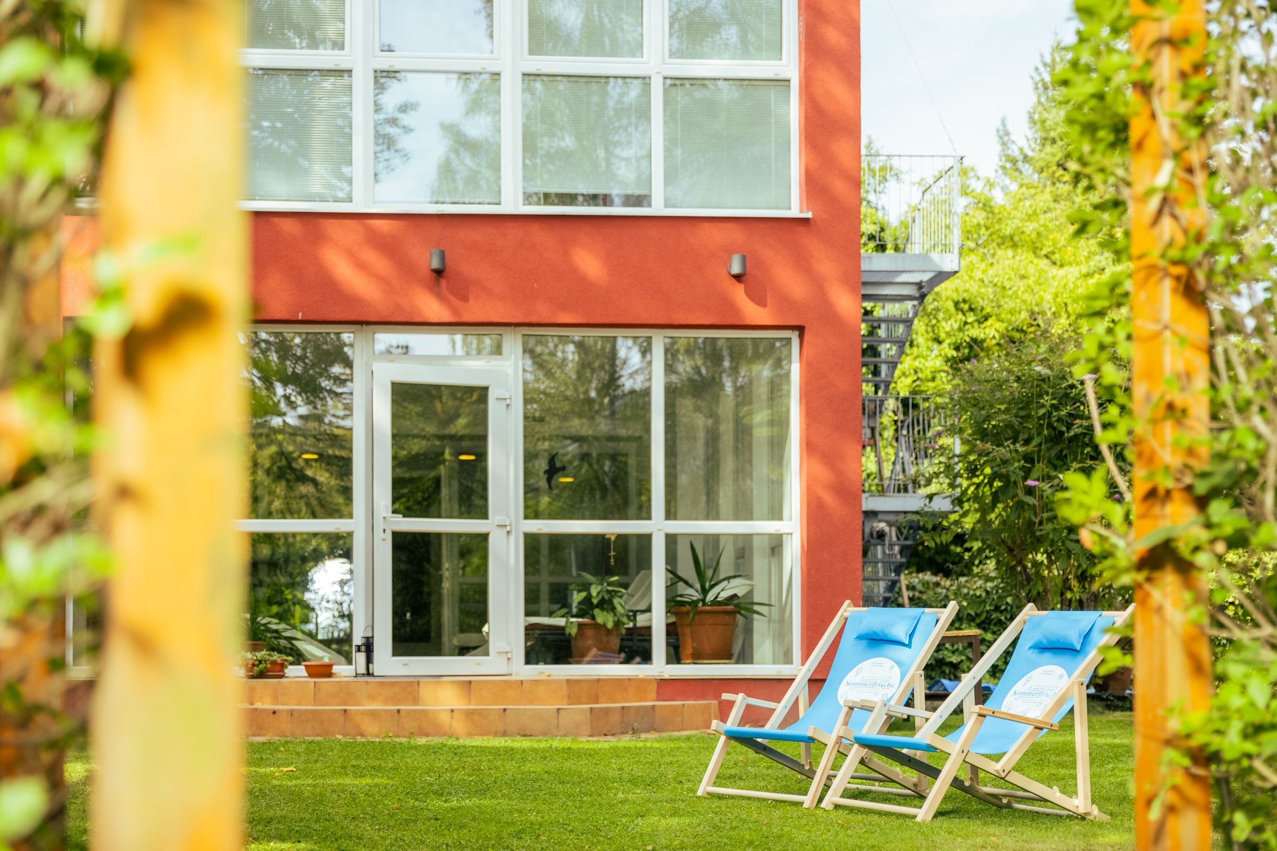 Two blue deckchairs on a green lawn in front of a red building with large windows.