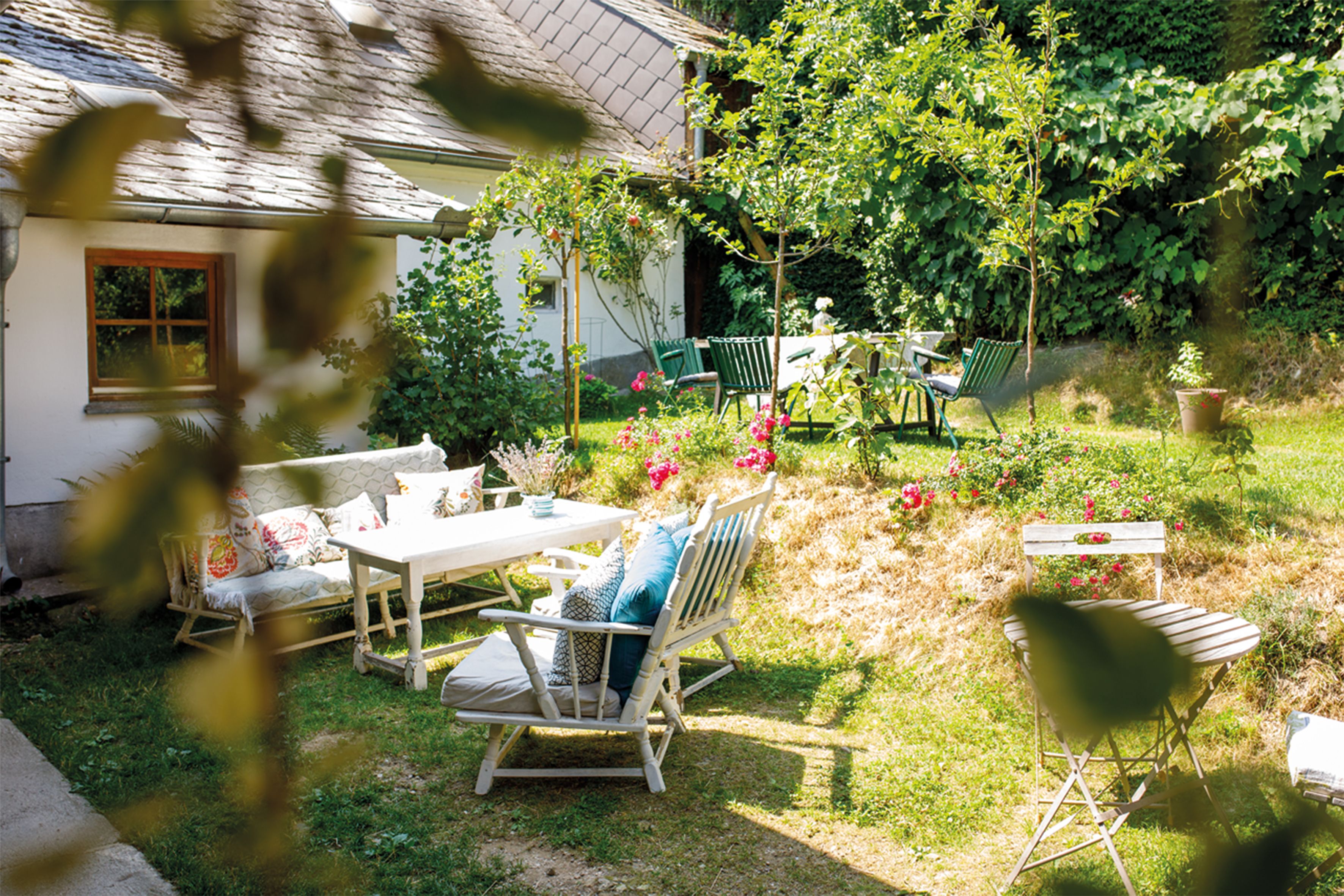 A cozy garden with outdoor furniture, flowers, and trees in front of a house.