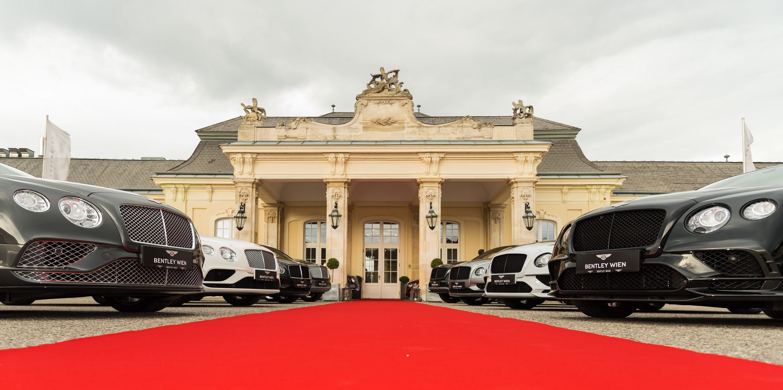 Luxury cars in front of a historic building with a red carpet.