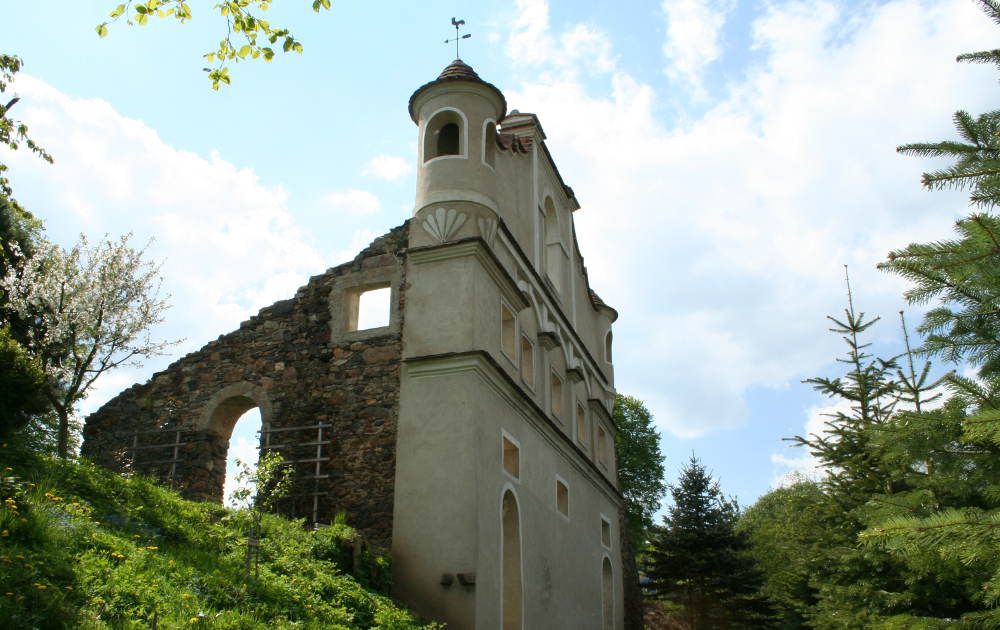 Ruins of a castle with preserved tower and remains of walls, surrounded by trees and blue sky.