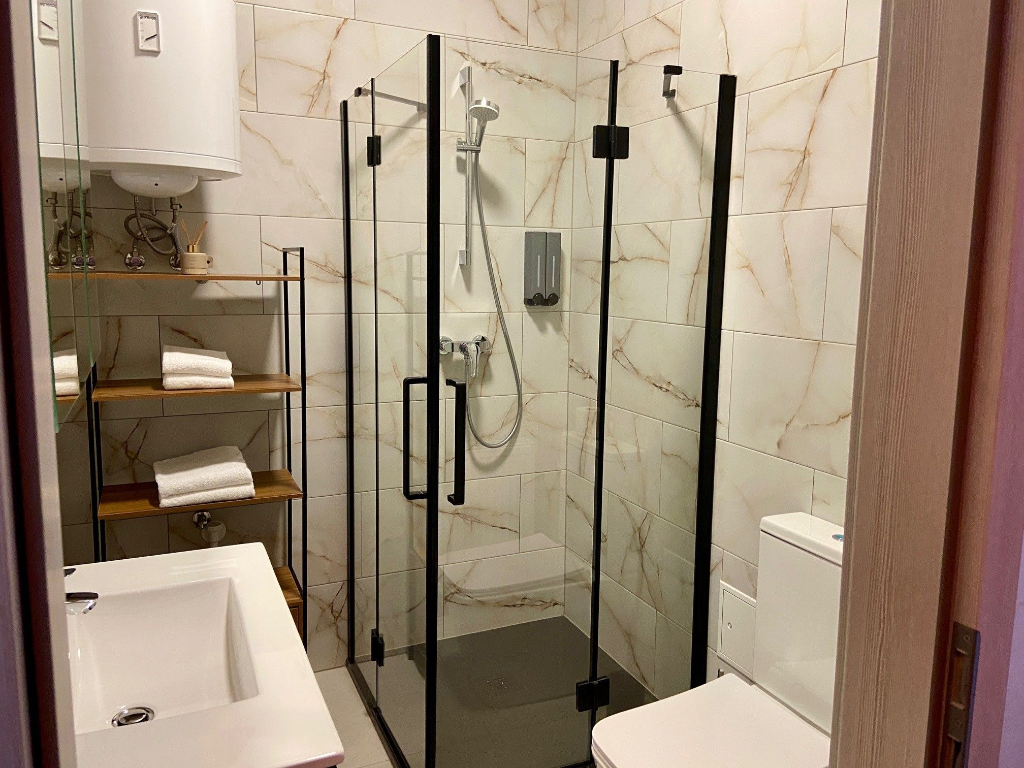 Modern bathroom with glass shower, washbasin, WC and shelf with towels.