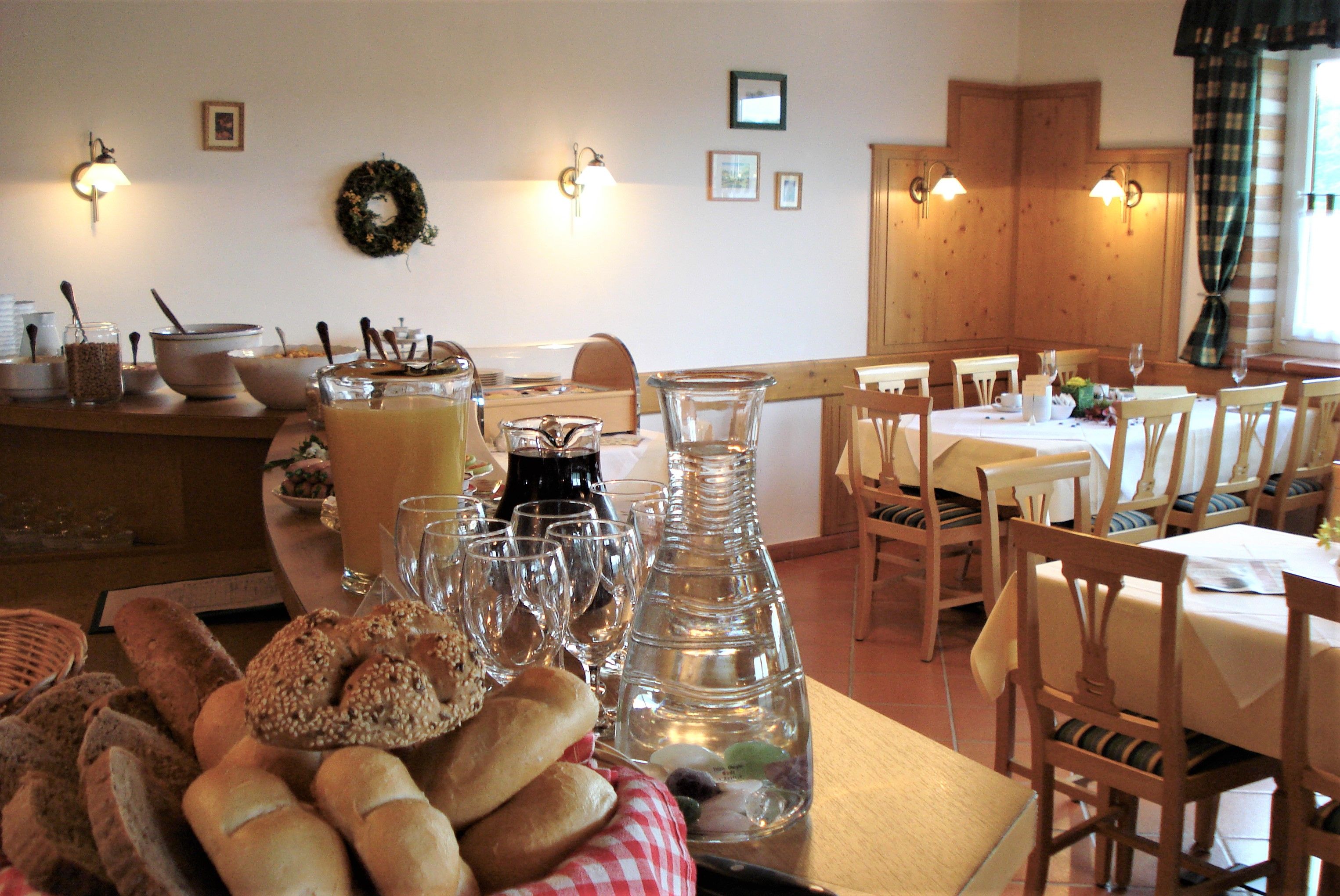 A breakfast room with laid tables, bread basket, juice and water jug on a buffet.