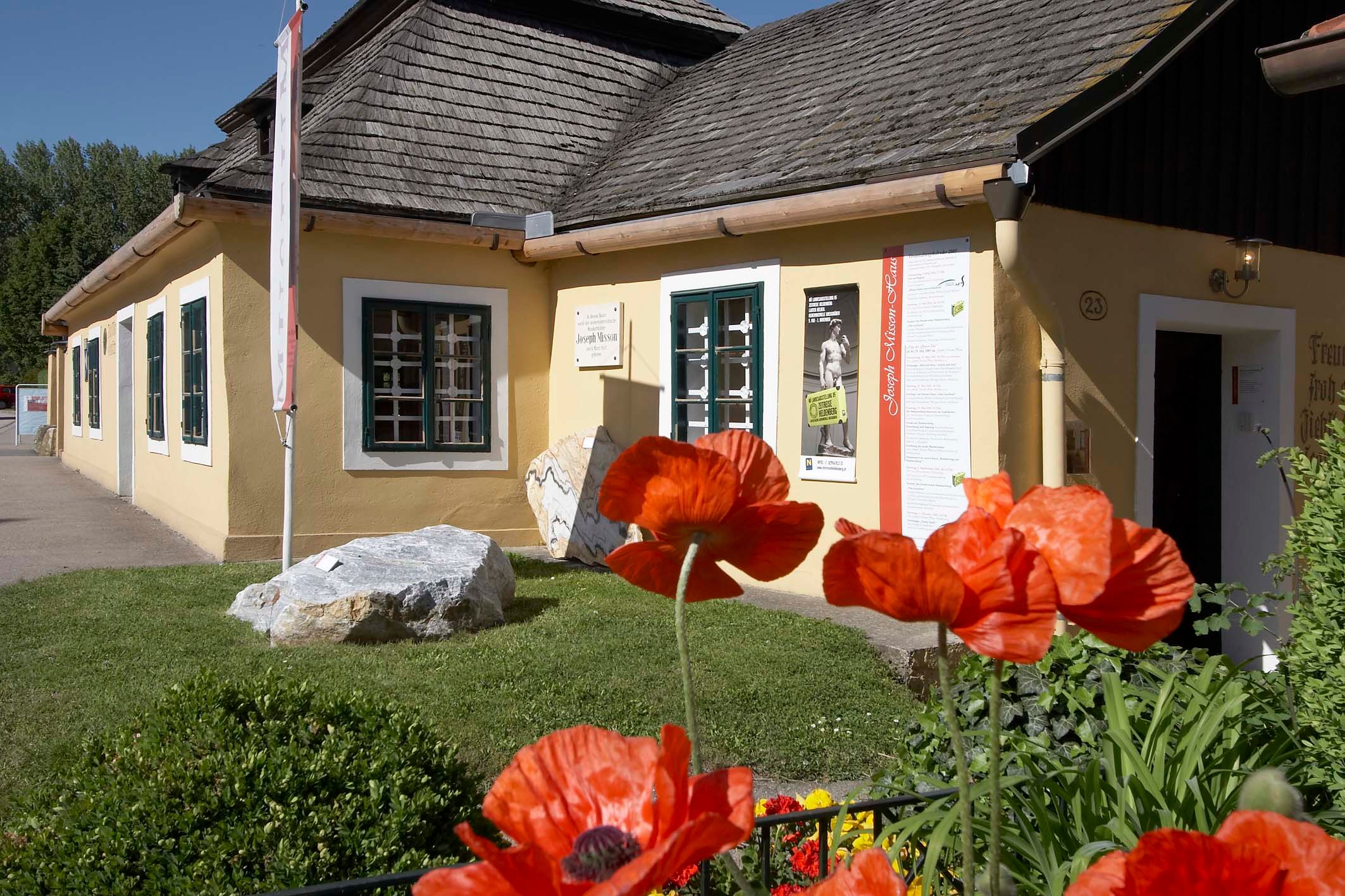 Yellow house with shingle roof and poppies in the foreground.