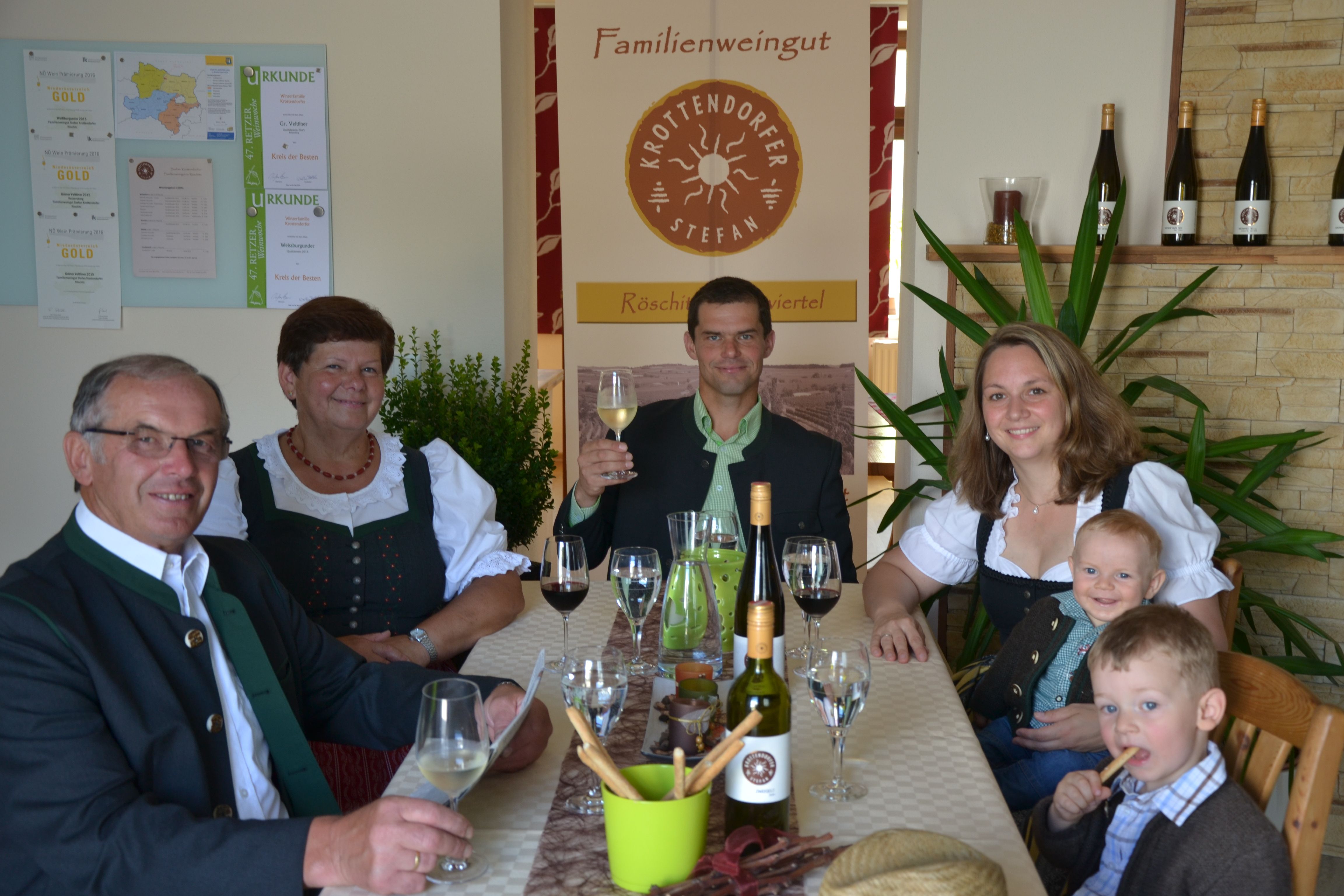 Family in traditional dress sitting at a table with wine and glasses.