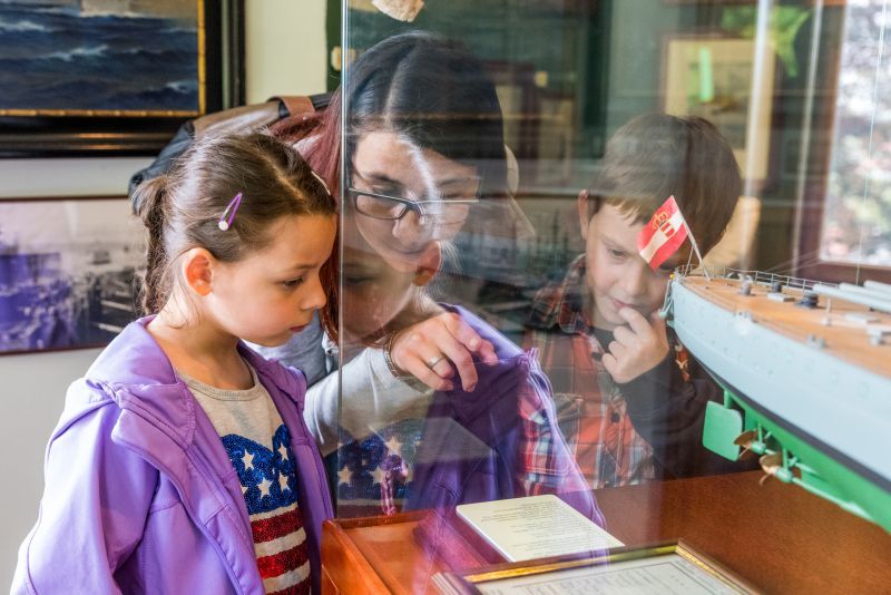Children look at a model ship in a museum.