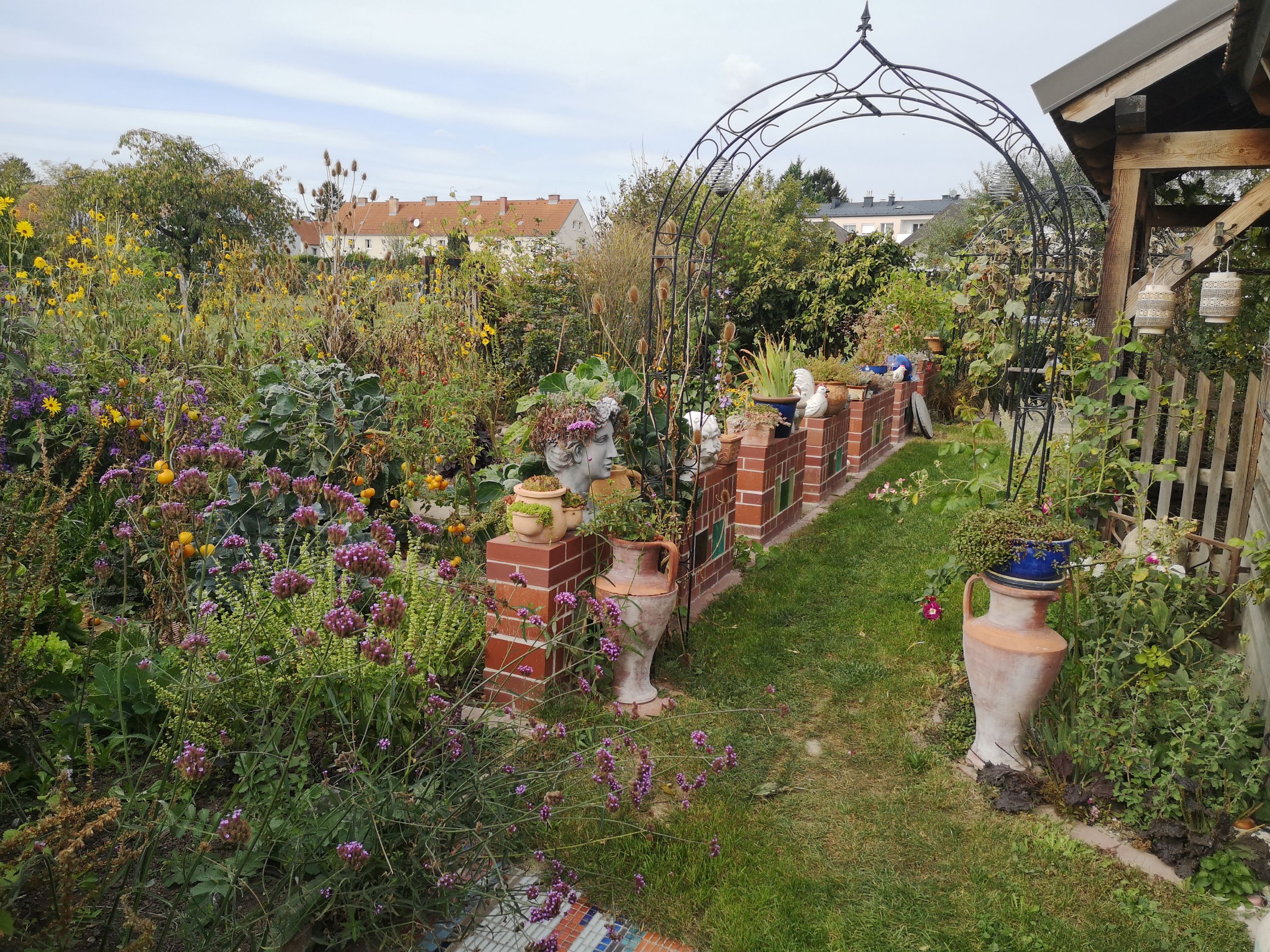 A colorful garden with flowers, brick wall and decorative vases.