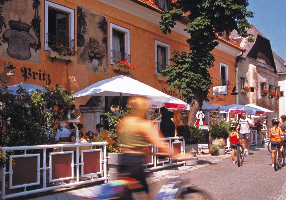 Cyclists in front of a hotel with a terrace and parasols.