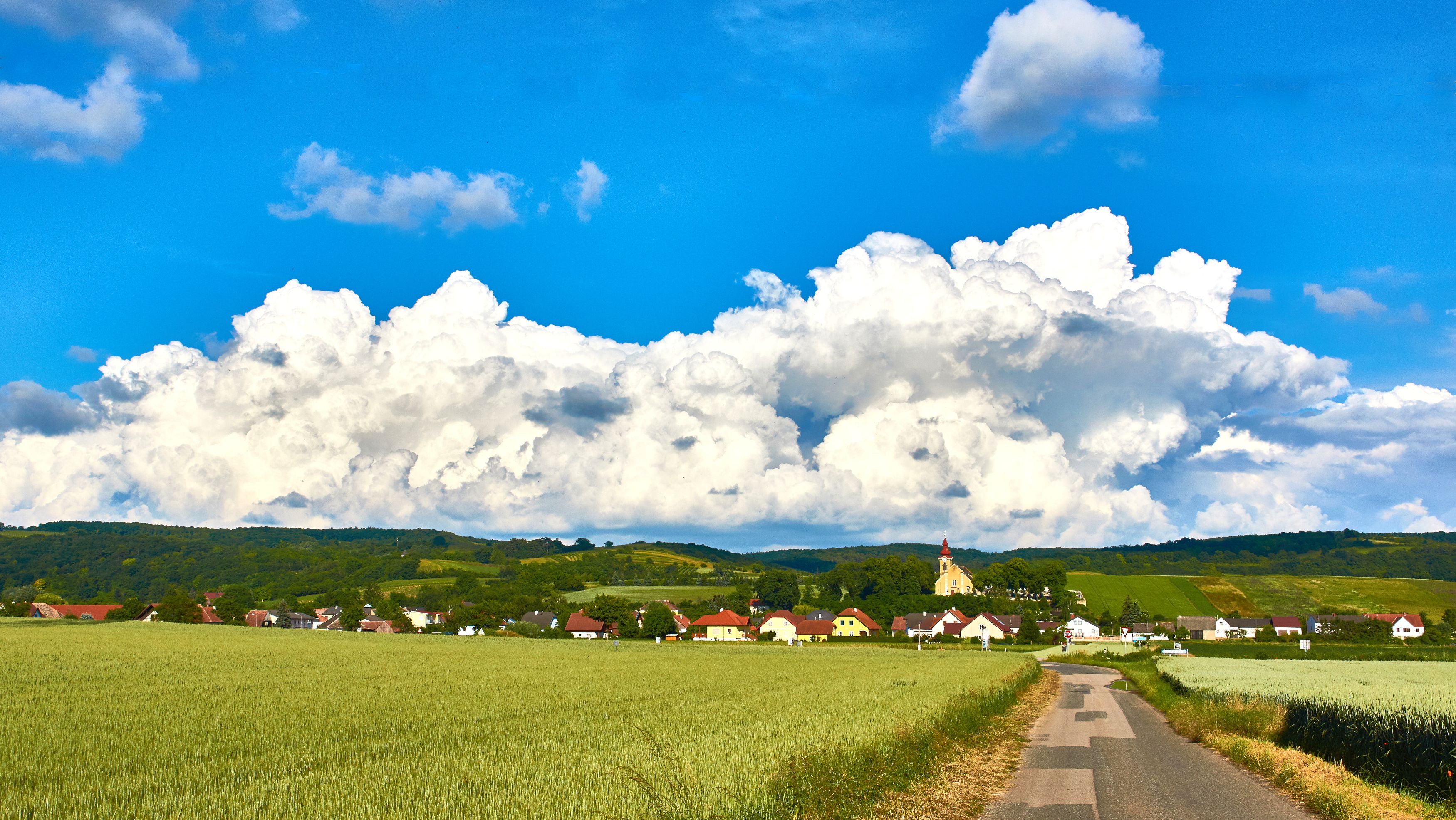 Landscape with village, fields and church in front of large clouds.