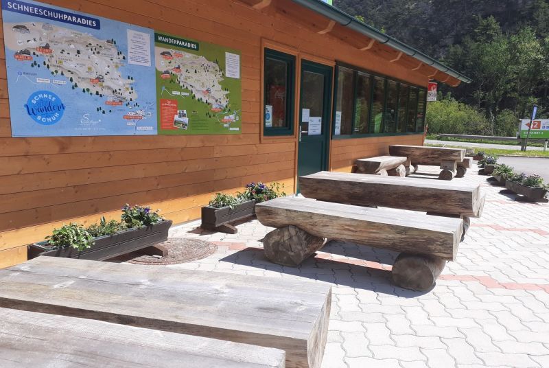 Wooden benches in front of a building with maps on the wall.