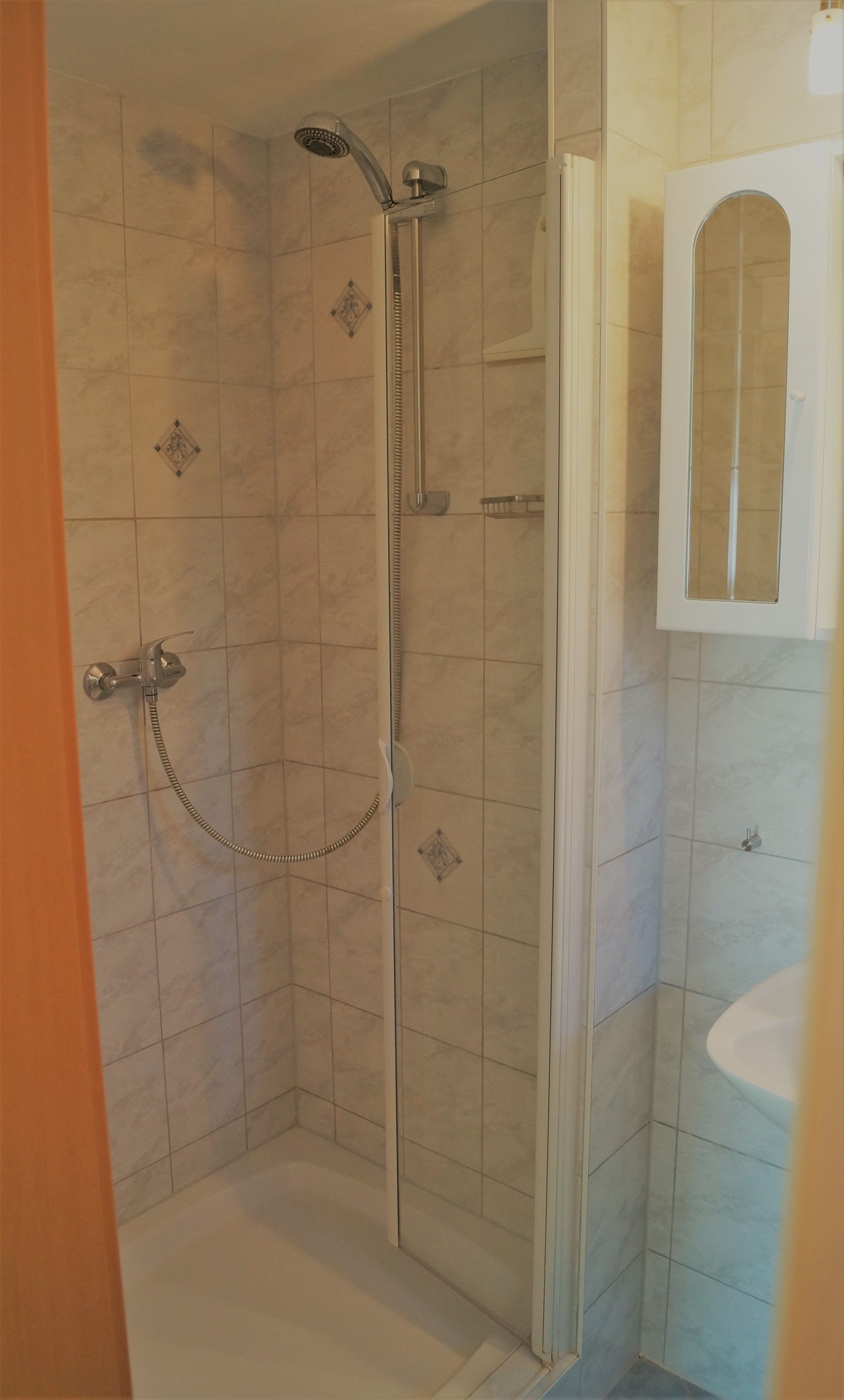 Small shower cubicle with tiles and shower head.