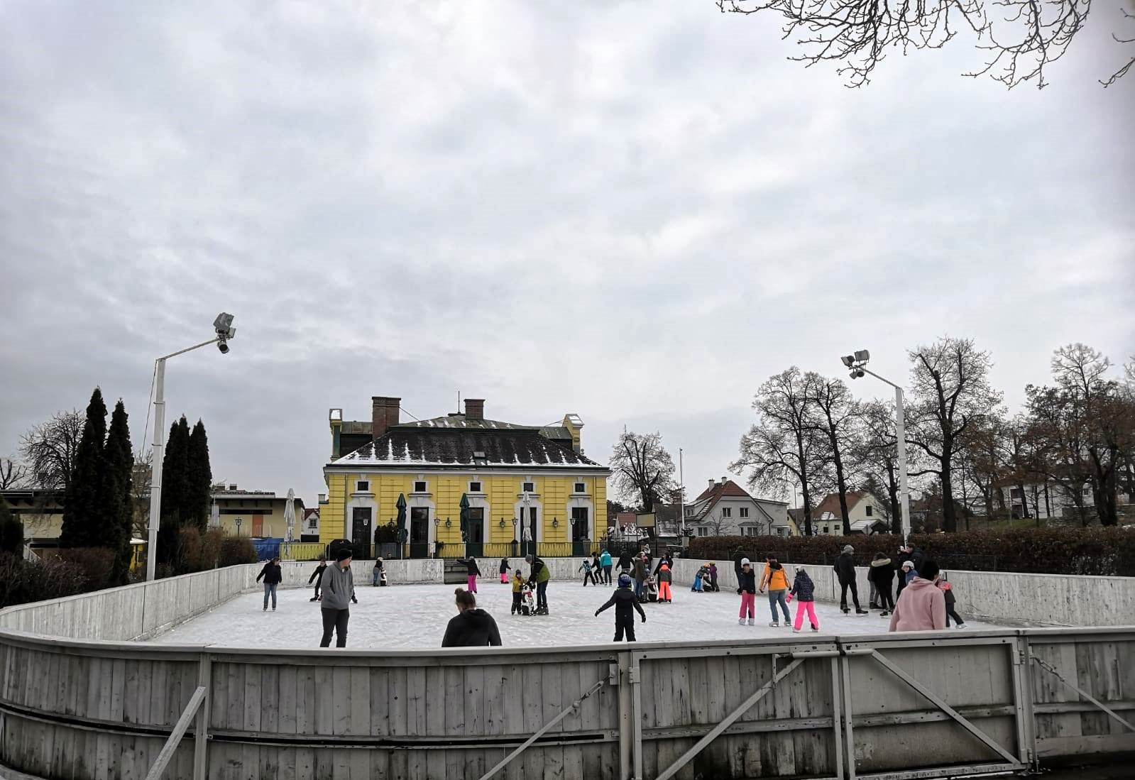 People skating on an open-air rink in front of a yellow building.
