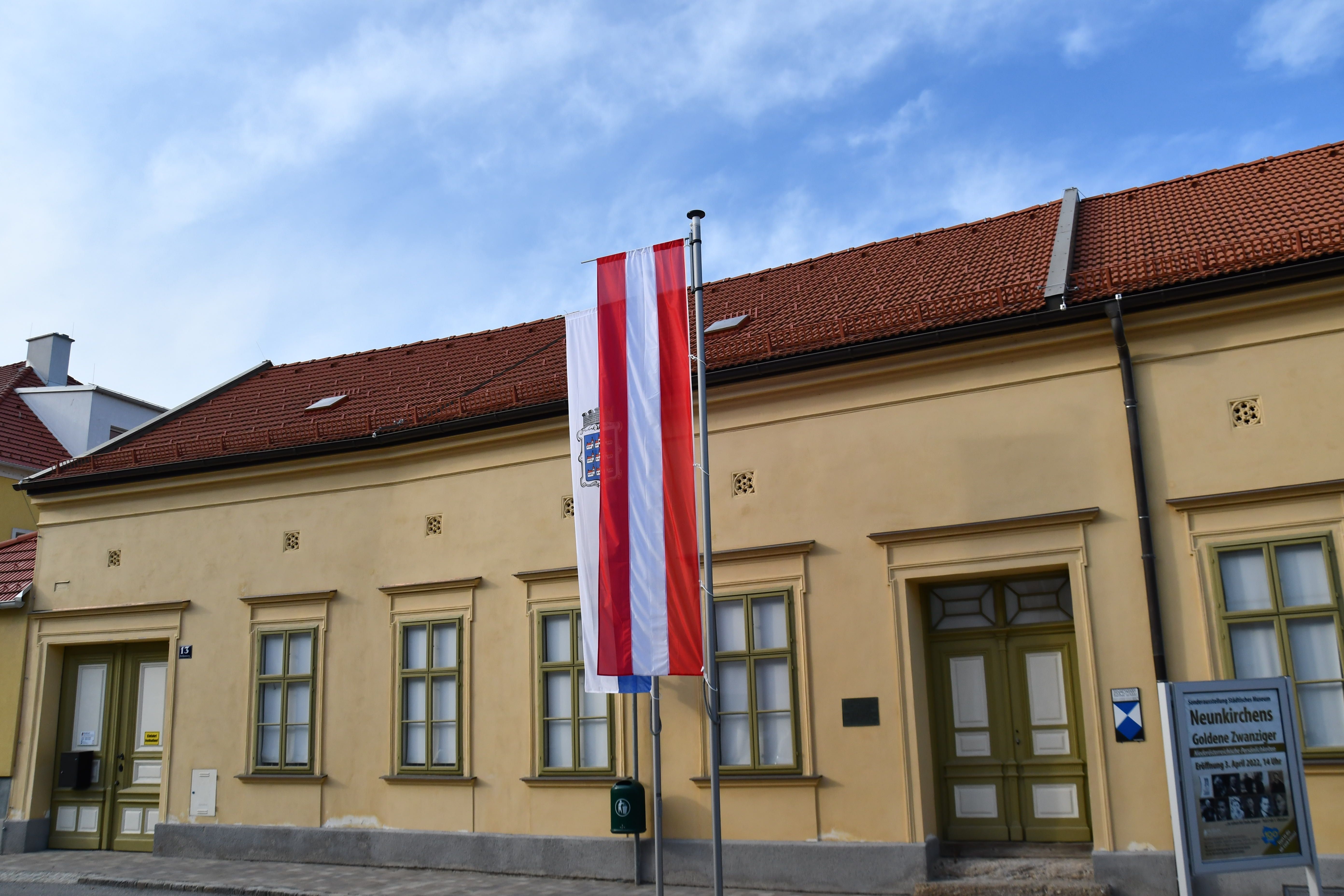 Exterior view of the Neunkirchen Museum with Austrian flag and information sign.