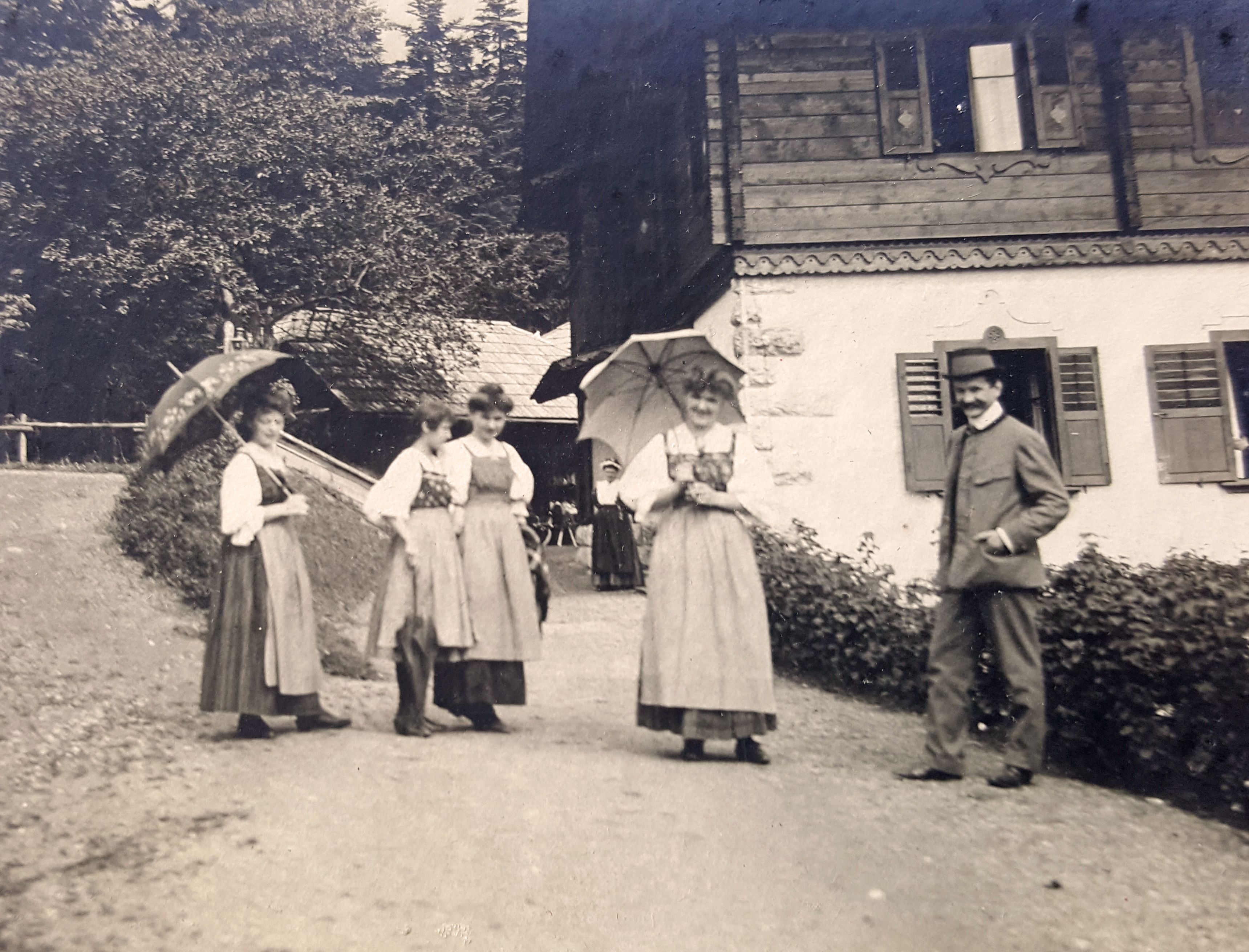 Black and white picture with women in long dresses and on the right a man in a hunting suit and hat 