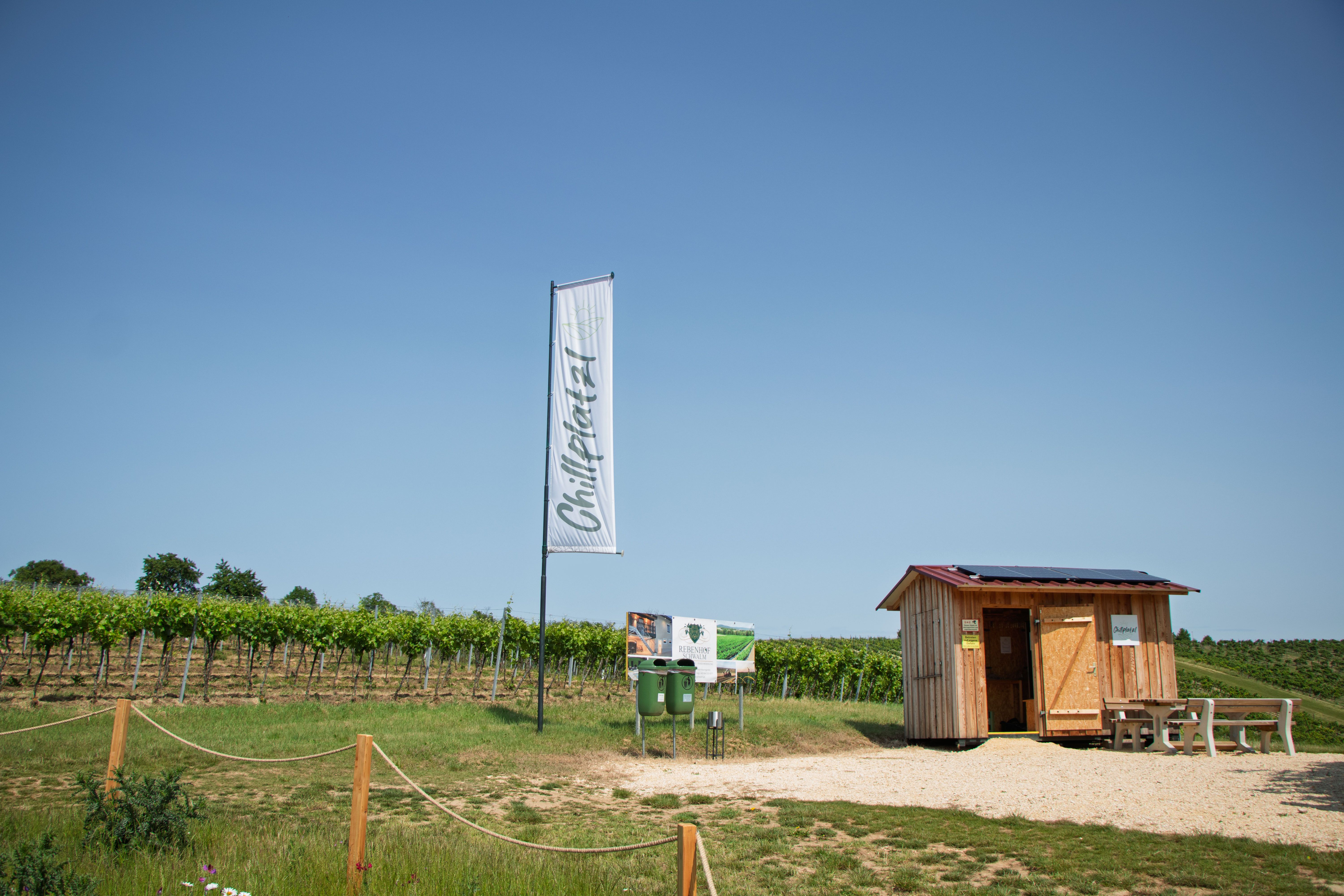 A small wooden shed next to a vineyard, with a sign and a flag that reads "Chill Spot."