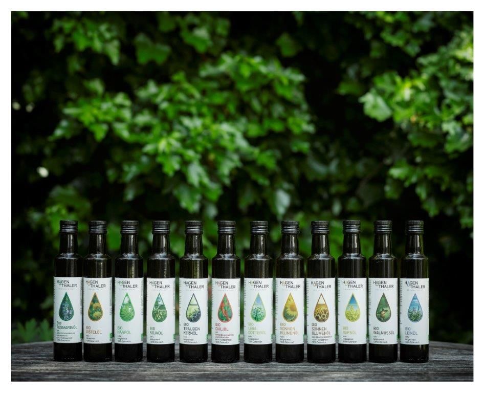 A row of oil bottles from Hagenthaler Ölmanufaktur in front of green foliage.