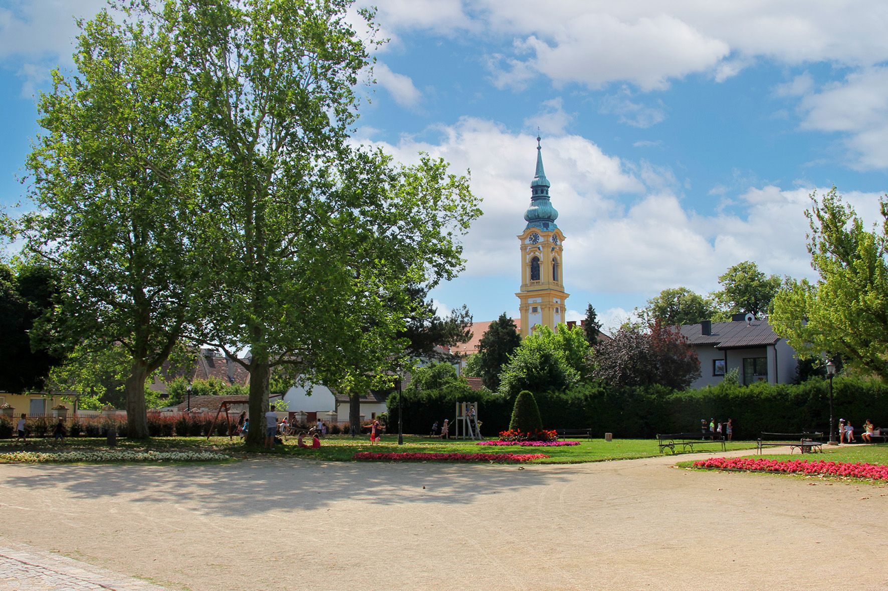 A park with trees, flowerbeds and a church tower in the background.